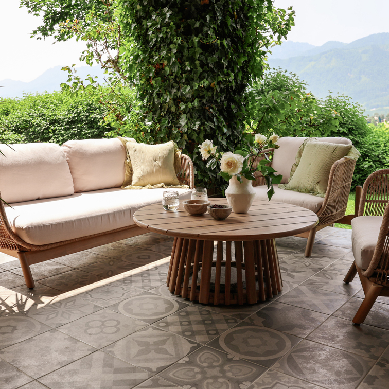 Tuinmeubilair van rattan met beige kussens en ronde houten tafel op terras met decoratieve tegels