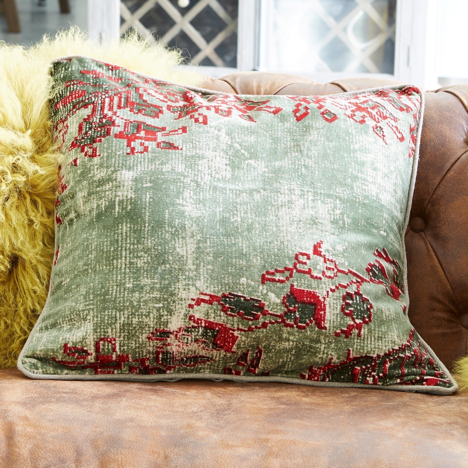 Coussin décoratif vert et rouge en tissu doux posé sur un canapé en cuir marron
