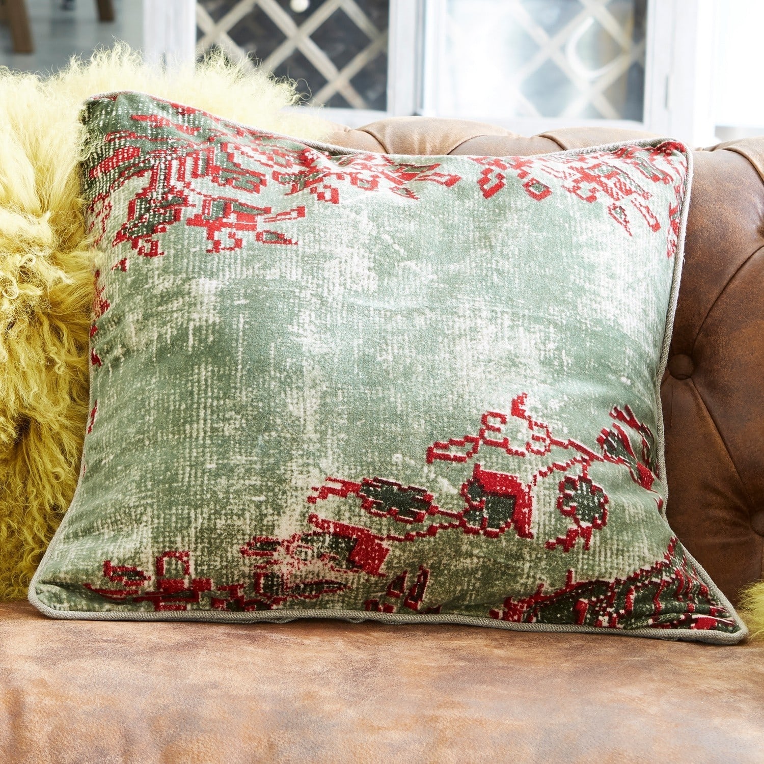 Coussin Vianney Coussin décoratif vert et rouge en tissu doux posé sur un canapé en cuir marron
