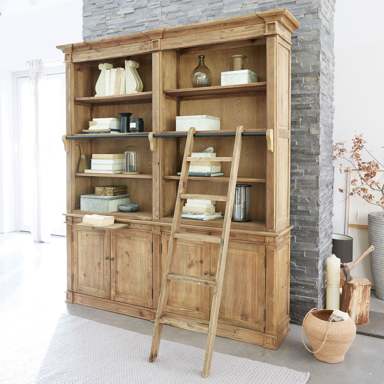 Grande bibliothèque en bois avec échelle et étagères remplies de livres et décorations dans un intérieur lumineux