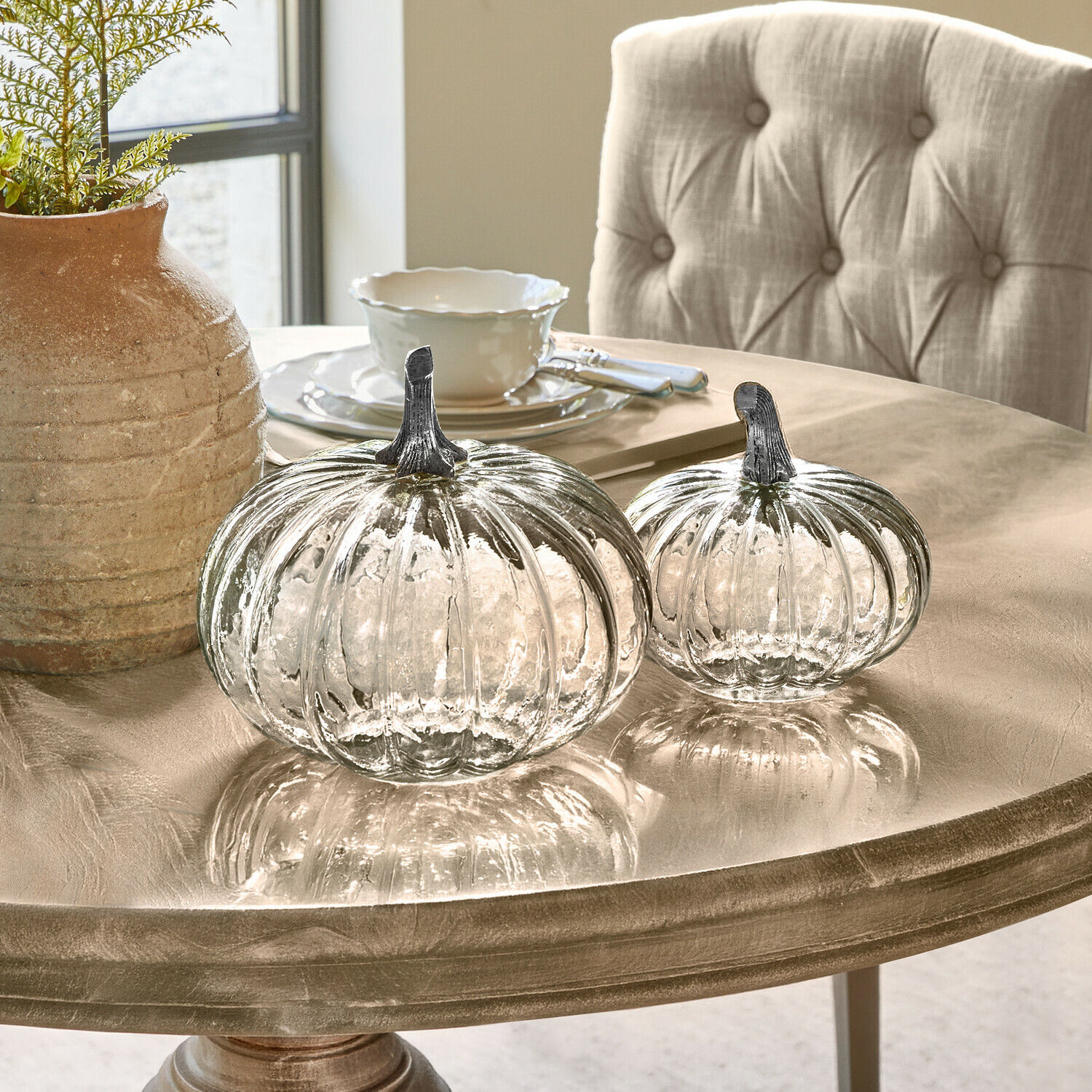 Pompoen set van 2 Perlouin Twee transparante glazen pompoenen met metalen stelen op een beige decoratieve tafel