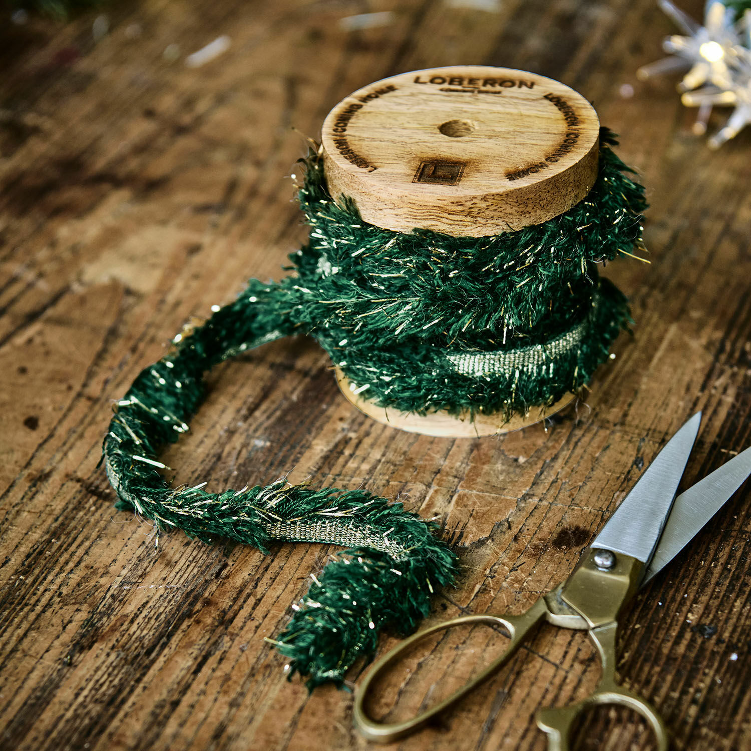 Ruban Calarith Ruban décoratif vert avec fils métalliques sur bobine en bois à côté de ciseaux sur table en bois