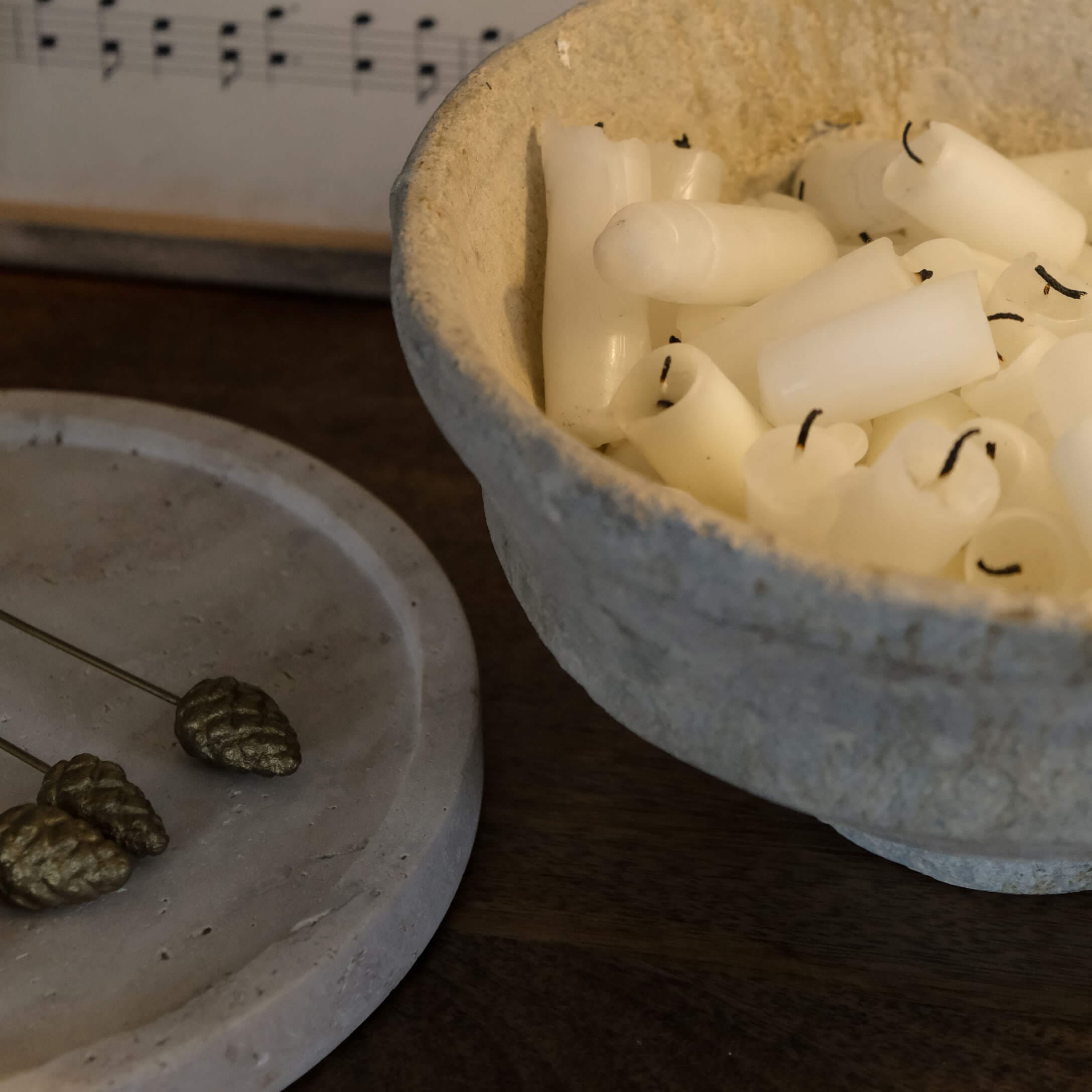 Bol en matériau naturel beige rempli de petites bougies blanches sur une table en bois foncé
