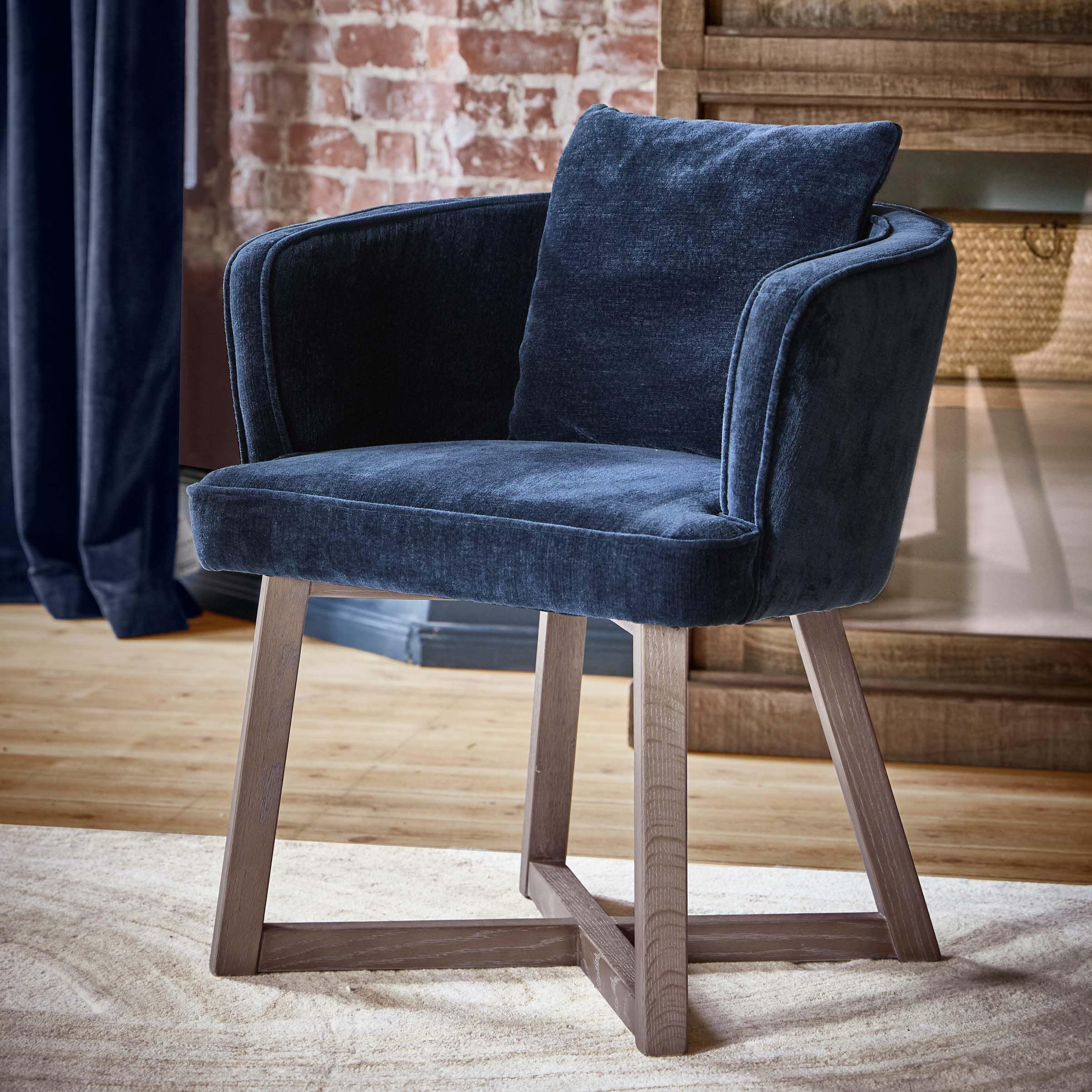 Donkerblauwe stoffen fauteuil met houten poten in stijlvolle kamer met bakstenen muur