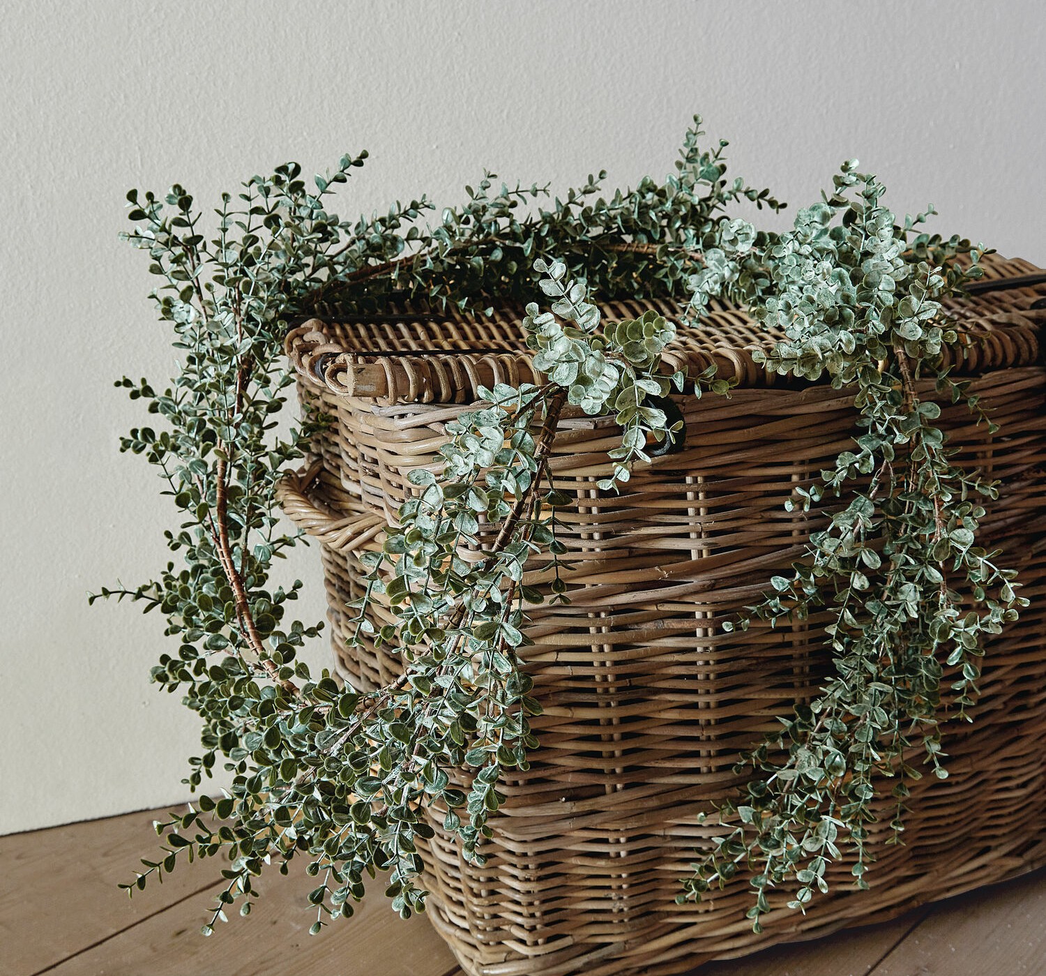 Couronne décorative en feuilles d'eucalyptus vertes posée sur un panier en osier sur un sol en bois