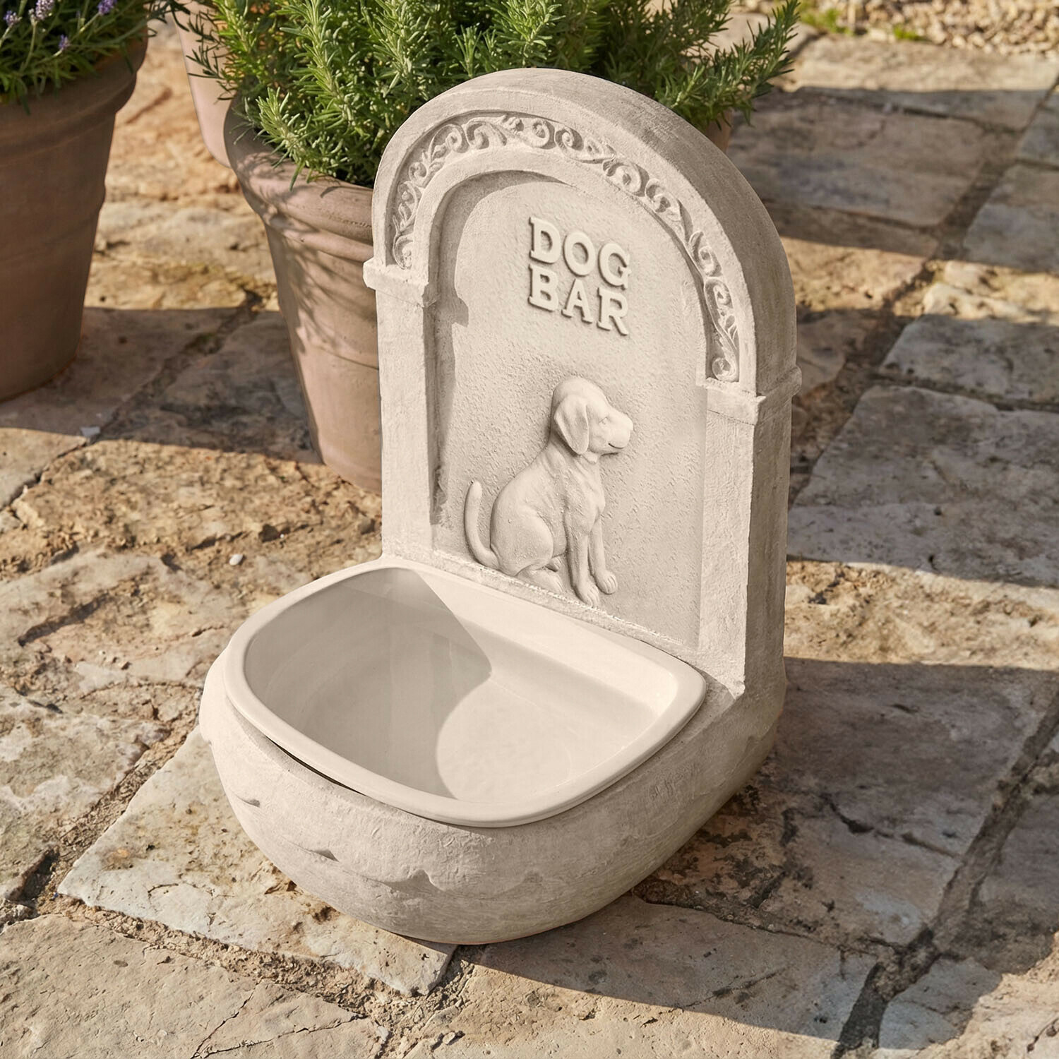 Grijze hondenbak van steen met hondendecoratie en tekst DOG BAR buiten