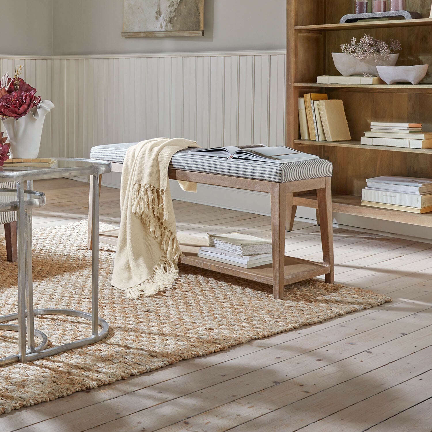 Banc Stormhavn Banc en bois avec assise rayée rembourrée et plaid crème sur tapis naturel dans un salon lumineux