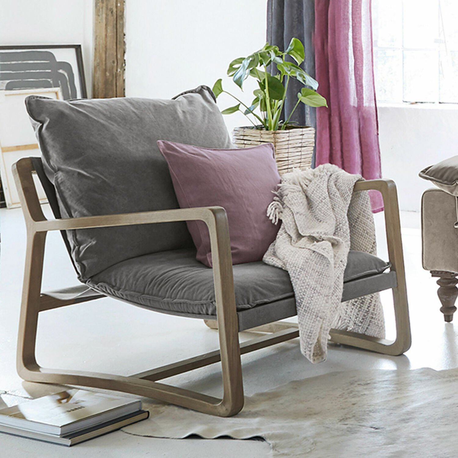 Fauteuil Jowna Fauteuil met grijze stof en houten frame, paarse kussen en beige deken in lichte kamer