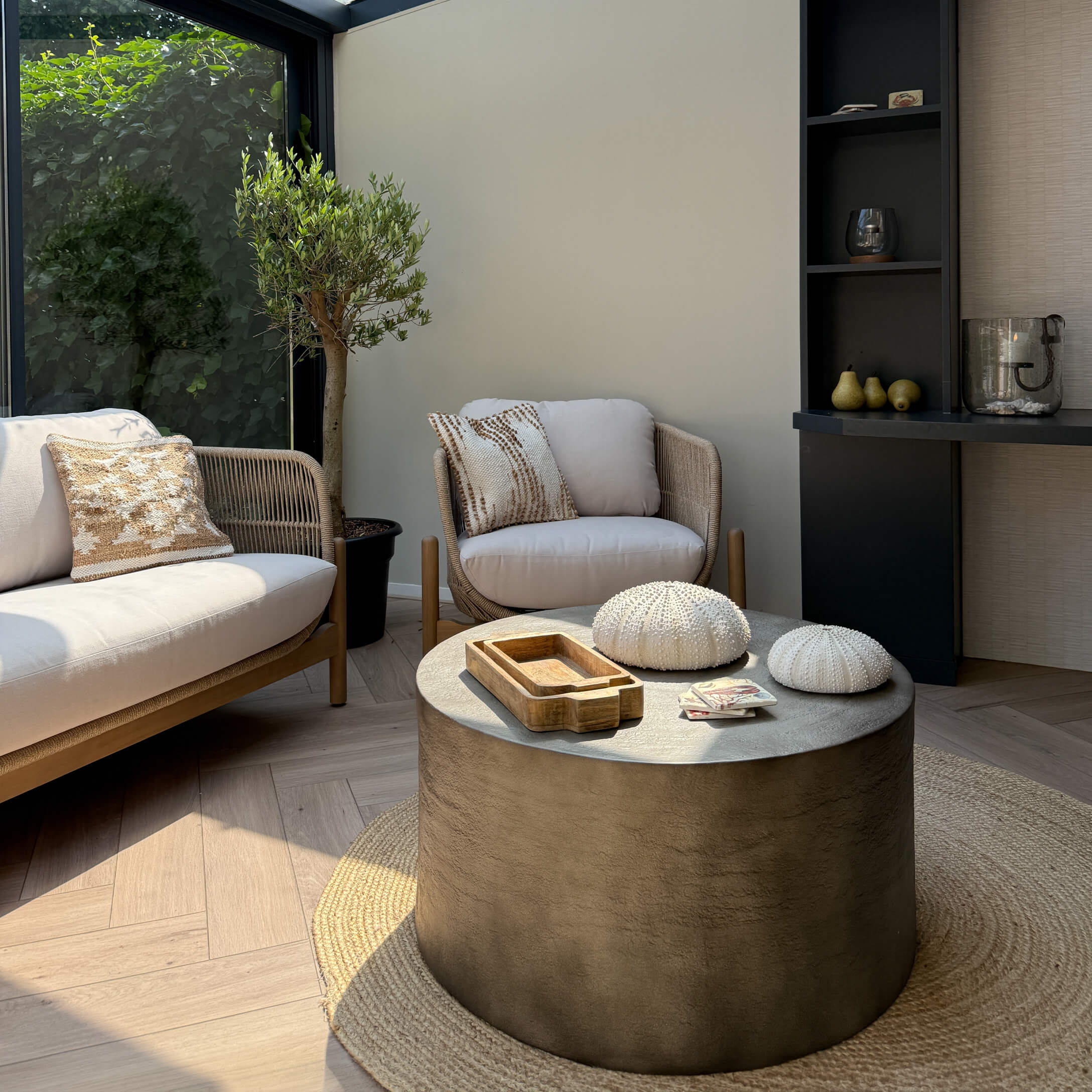 Moderne woonkamer met beige stoffen bank en fauteuil, ronde betonnen salontafel op natuurlijke vloerkleed