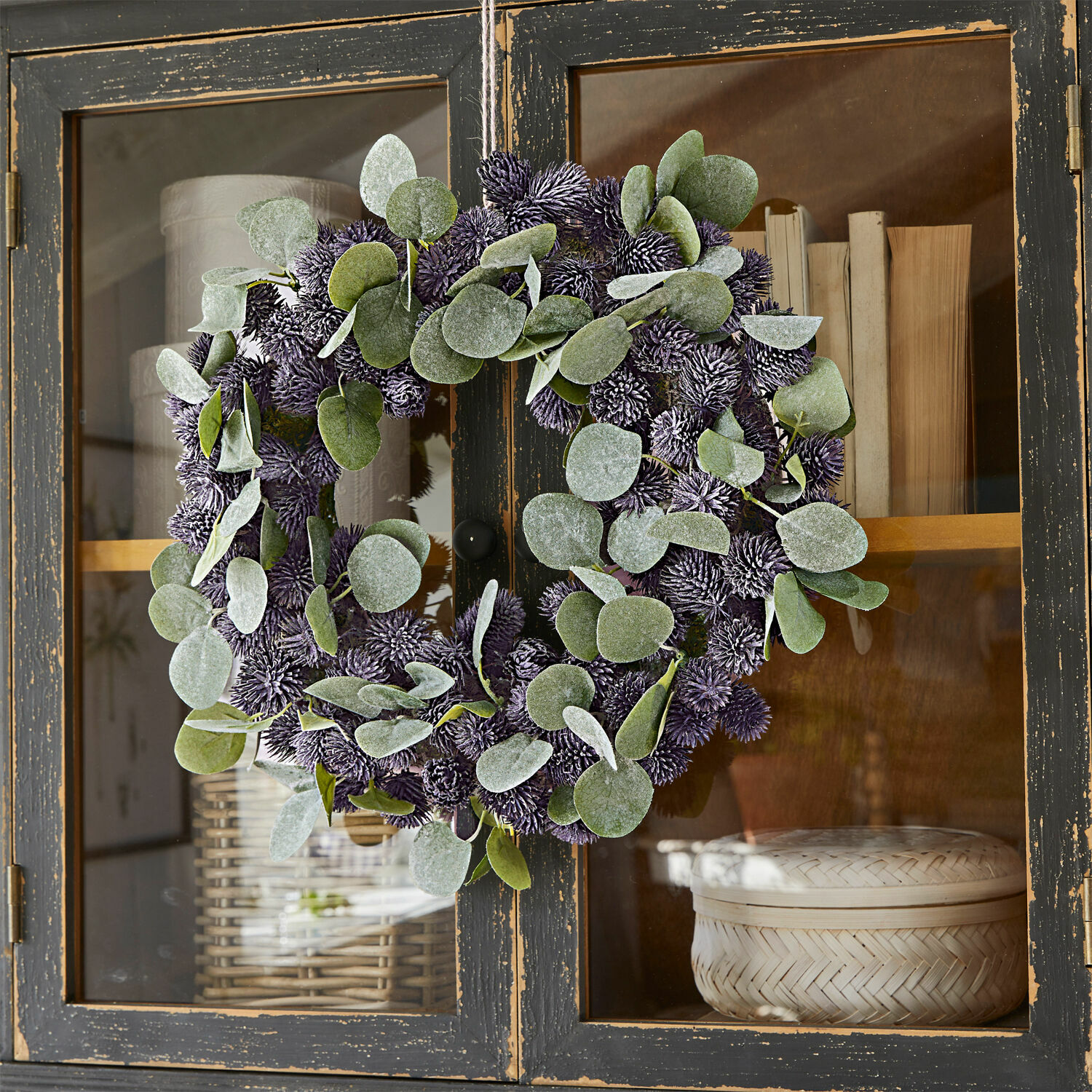 Couronne Épine Couronne décorative avec feuilles vertes et boules violettes suspendue à une armoire en bois noir