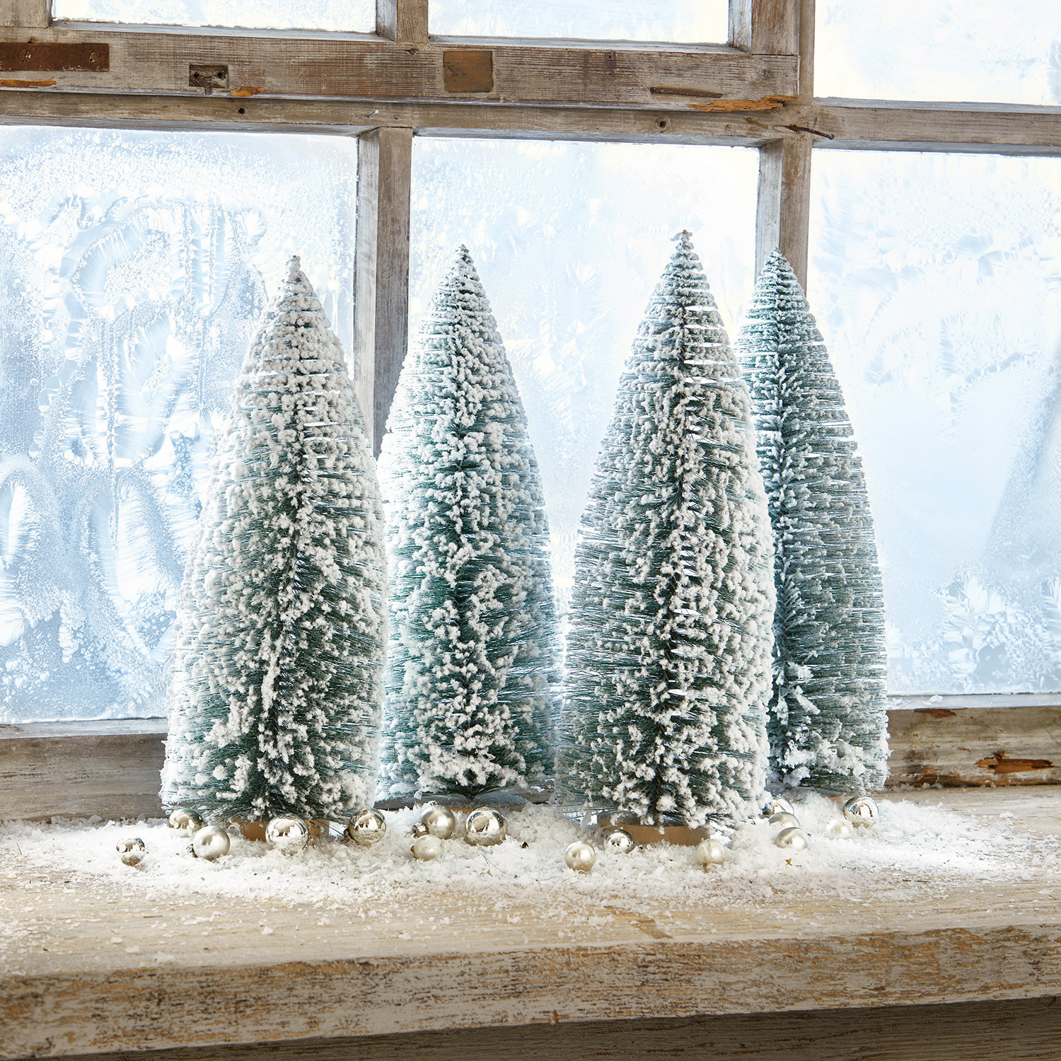 Sierboom set van 4 Landscape Vier groene kunststof kerstbomen in kegelvorm met witte sneeuw op een houten vensterbank met zilveren ballen