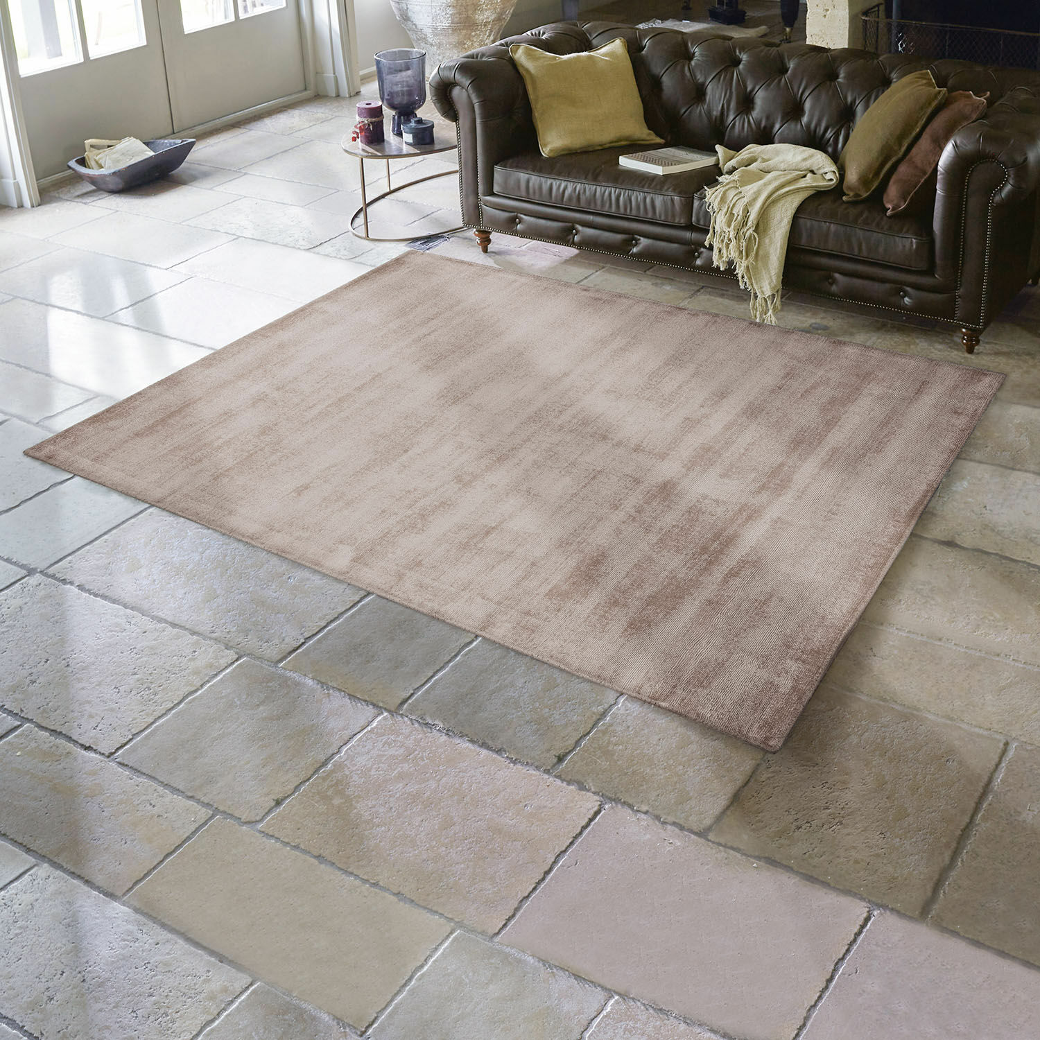 Vloerkleed Mariselle Beige vloerkleed van zacht materiaal op stenen vloer in woonkamer met bruine leren bank