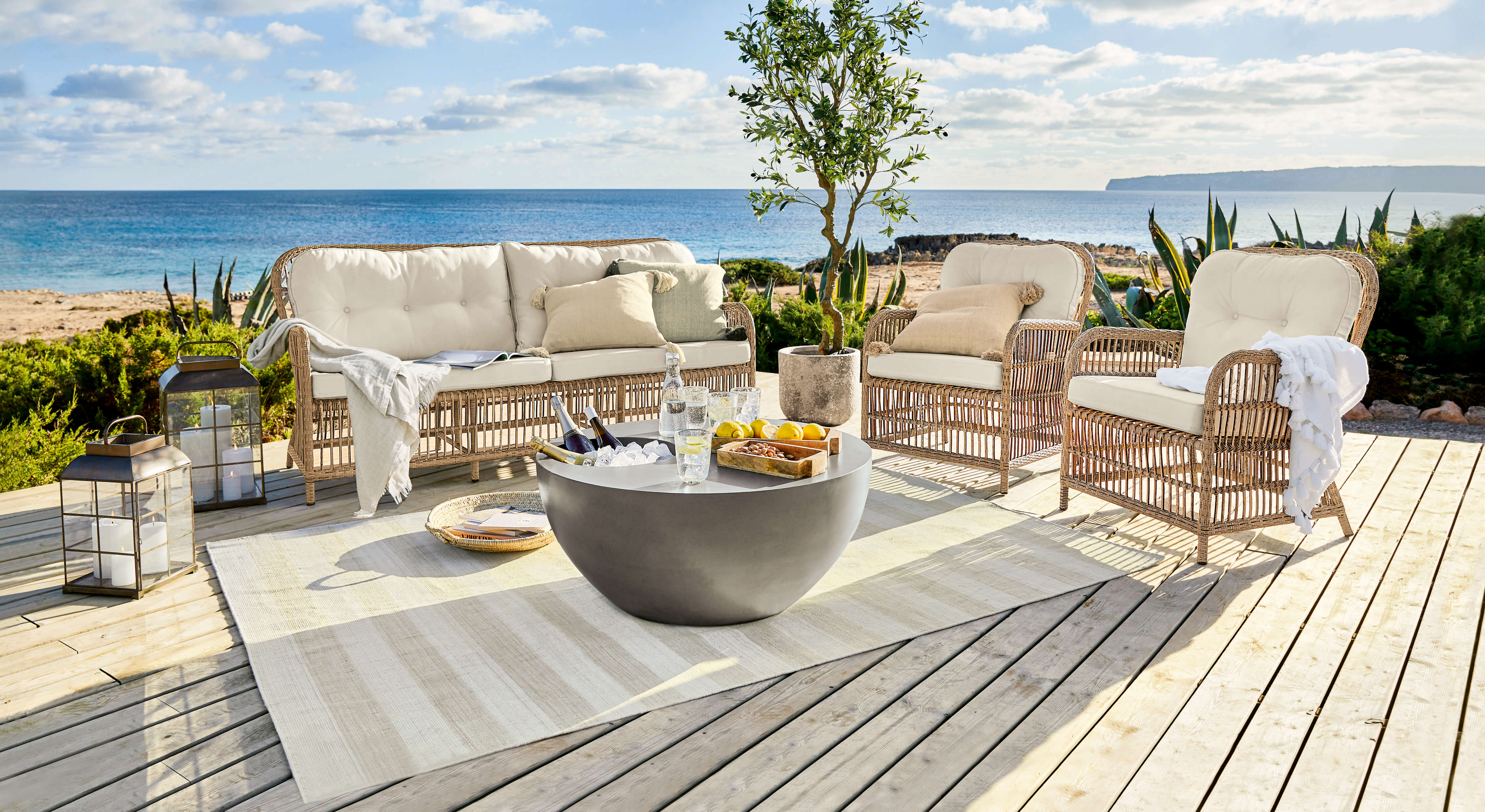 Rotan tuinmeubelset met crèmekleurige kussens op houten terras met zeezicht