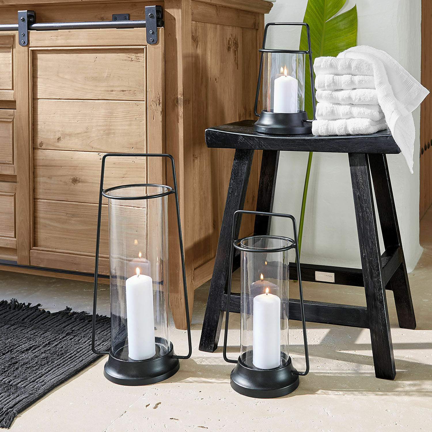 Lot de 3 lanternes Mirandel Ensemble de trois lanternes en métal noir avec bougies blanches et serviettes sur un tabouret noir