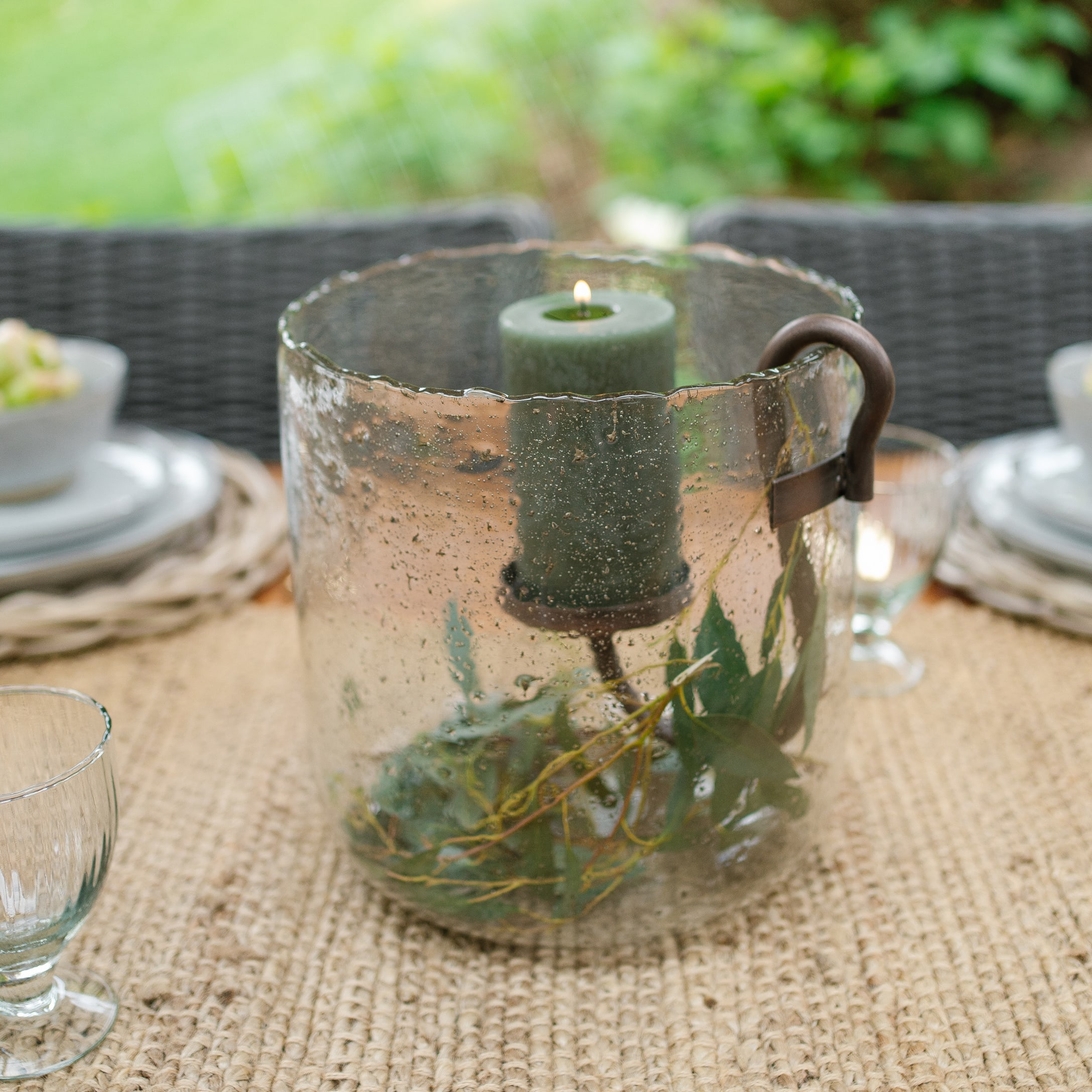 Photophore en verre avec bougie verte et poignée en métal sur une table rustique en extérieur