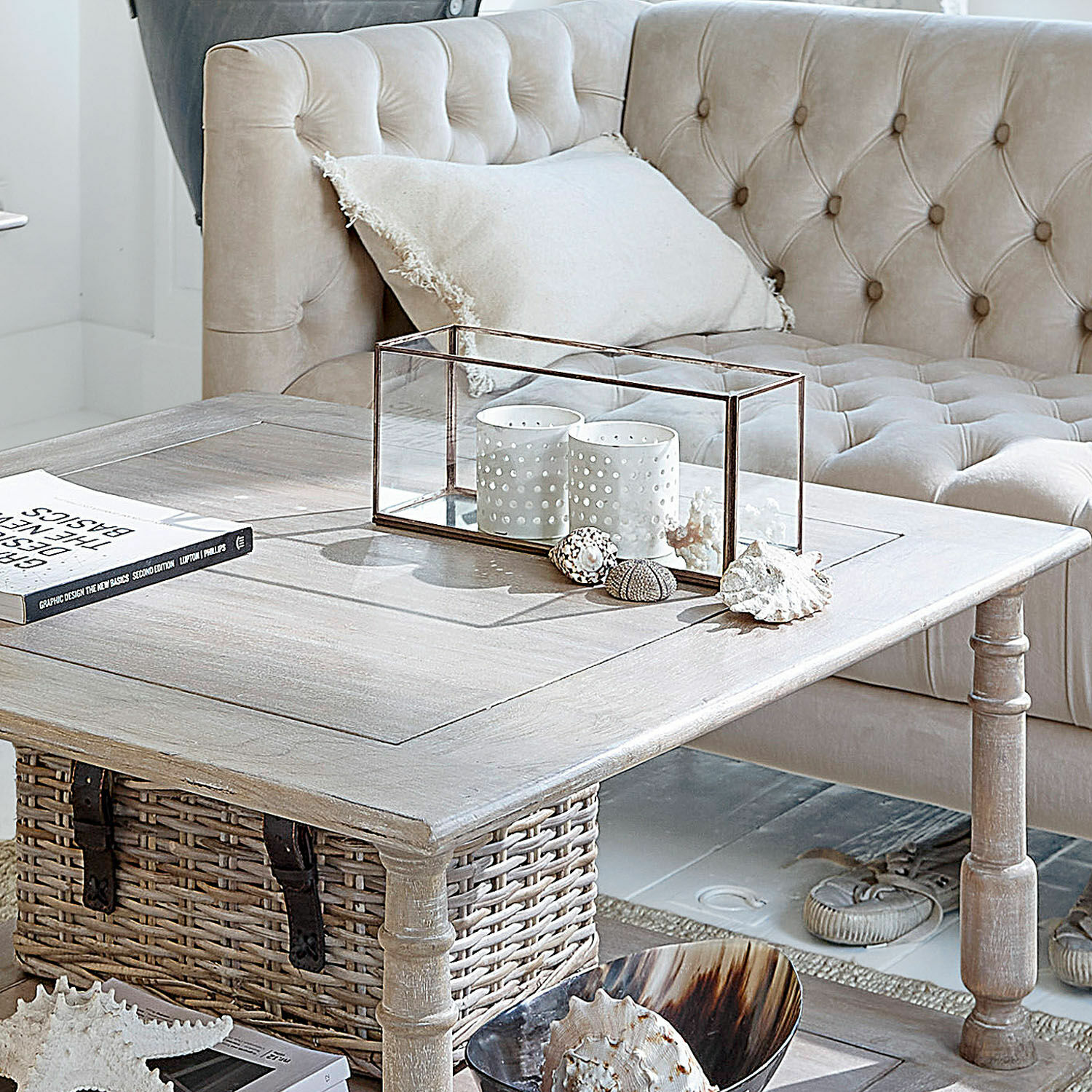Photophore Flavin Table basse en bois clair avec panier en osier et décorations sur canapé beige capitonné