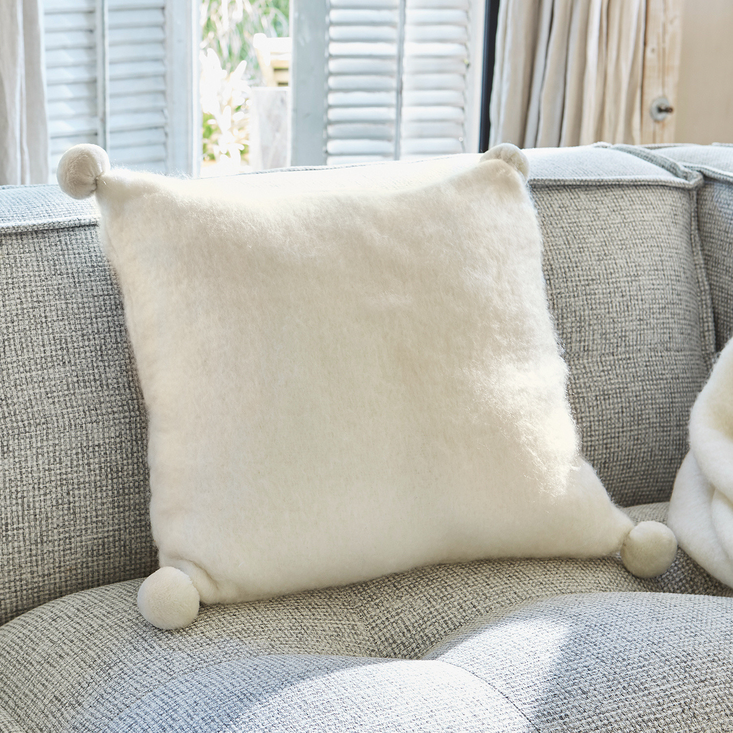 Coussin blanc doux en laine avec pompons sur canapé gris, décoration intérieure cosy