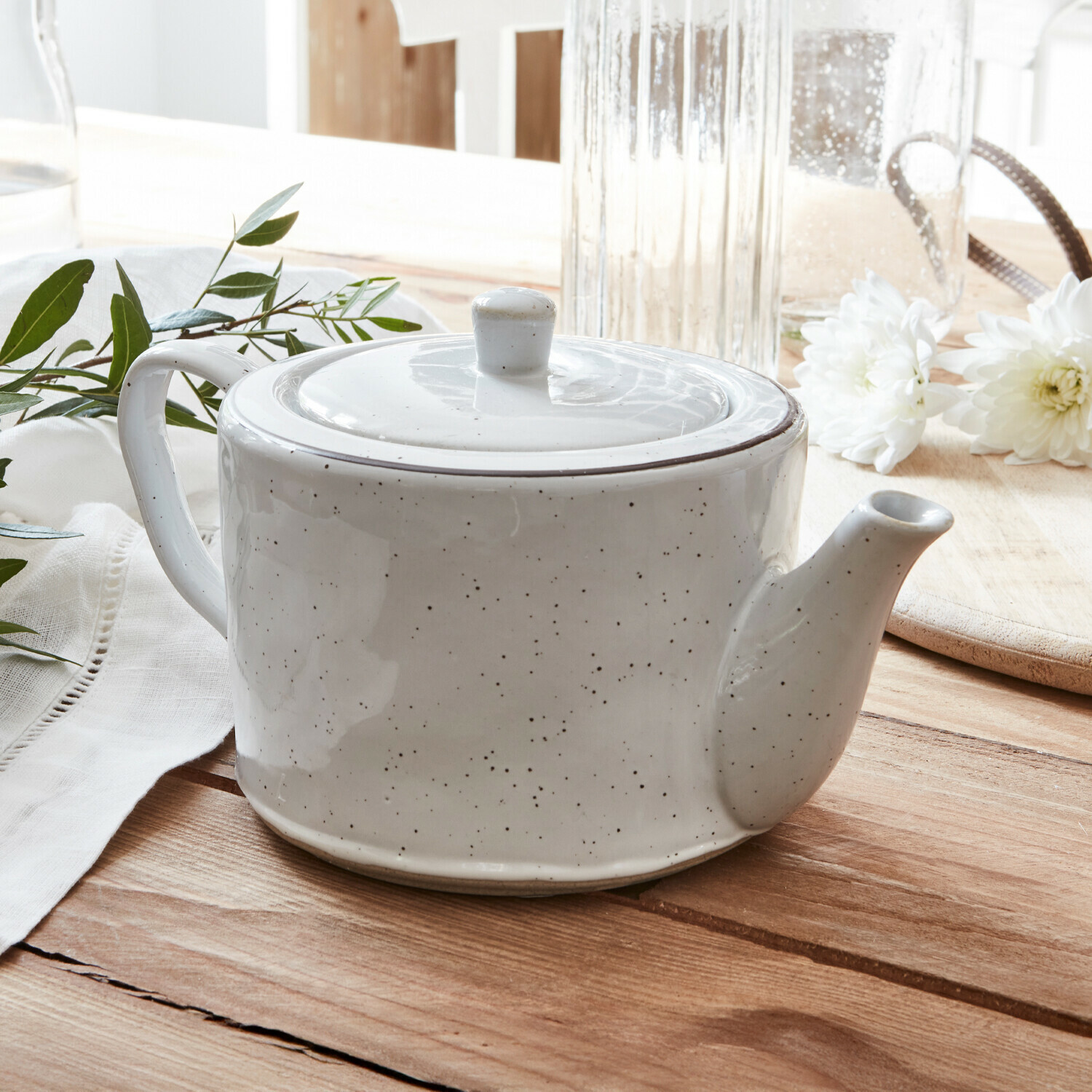 Théière Biarré Théière en céramique blanche avec couvercle sur table en bois décorée de fleurs blanches et feuilles vertes