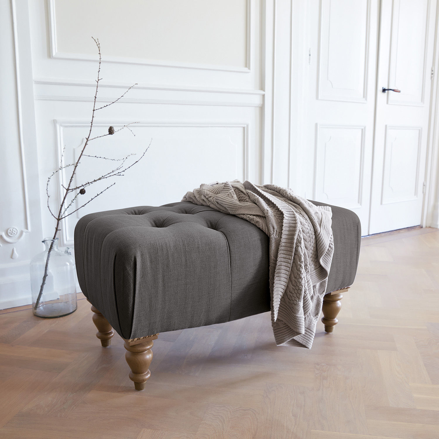 Hocker Durance Grijze gestoffeerde poef met houten poten en beige deken in lichte kamer