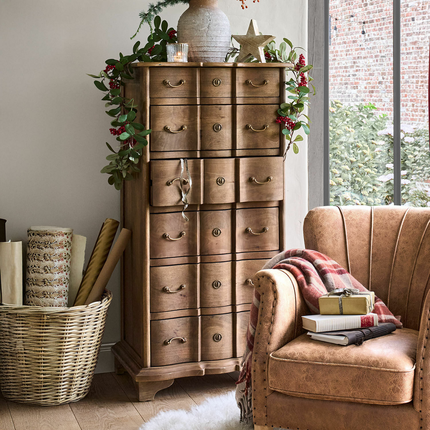 Chiffonnier Aiguillon Commode en bois avec poignées décoratives et guirlande de feuilles vertes et baies rouges dans un intérieur chaleureux
