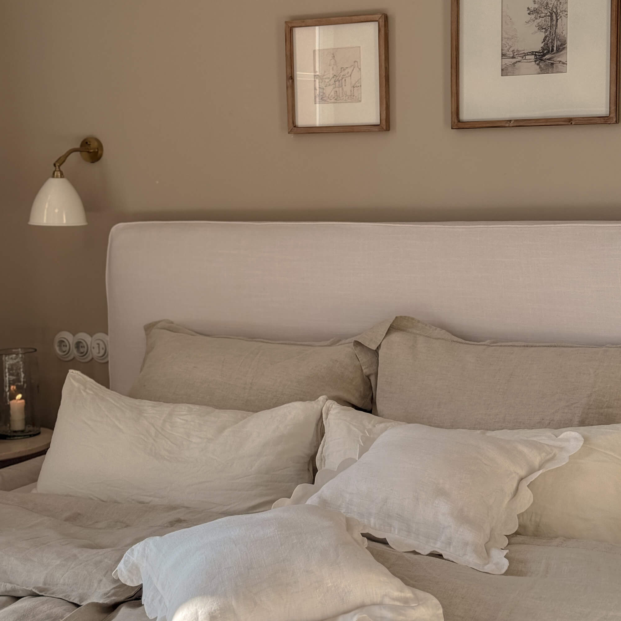 Gezellige slaapkamer met beige linnen beddengoed en licht gestoffeerd hoofdeinde