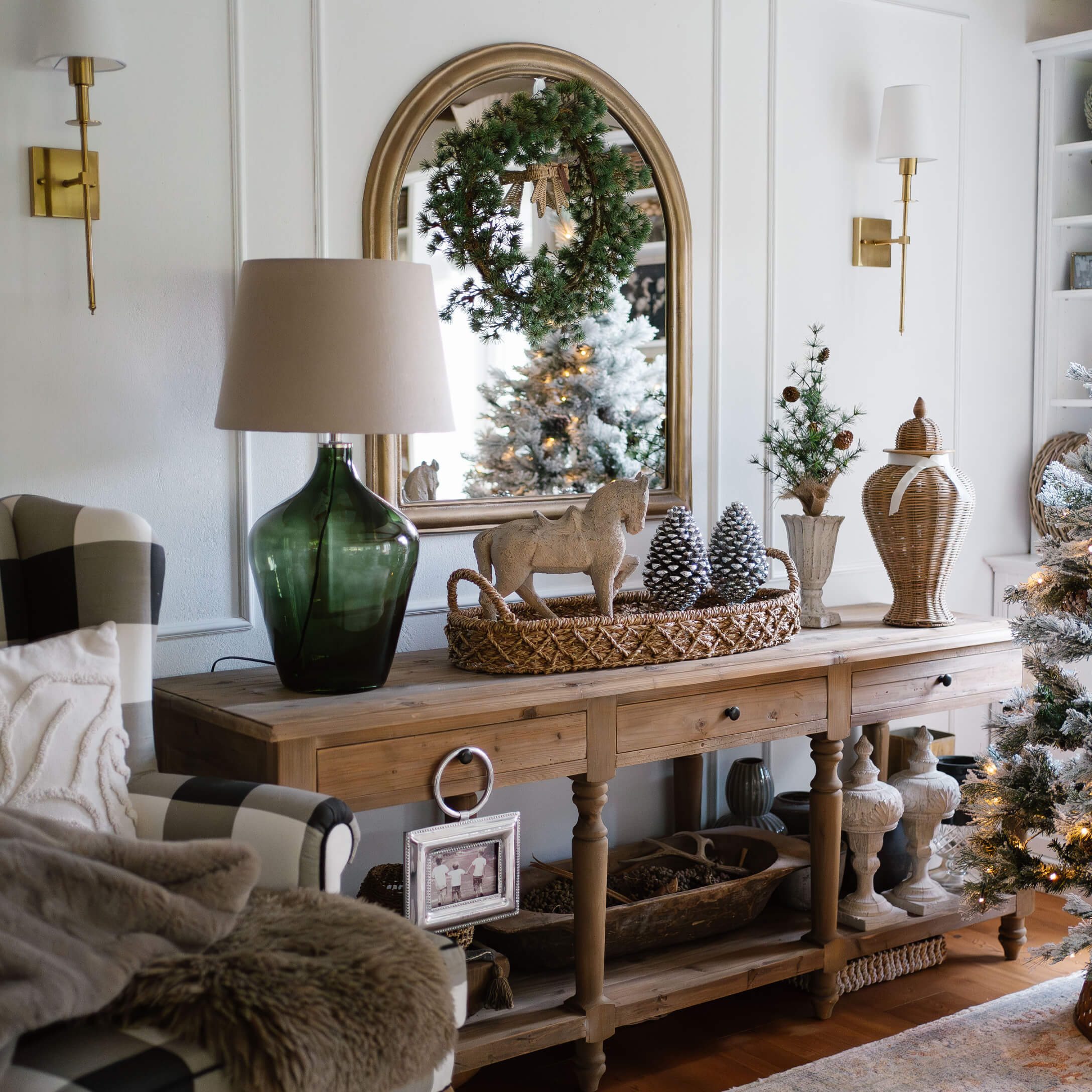 Table en bois avec décorations de Noël, lampe verte et miroir avec couronne dans un salon chaleureux