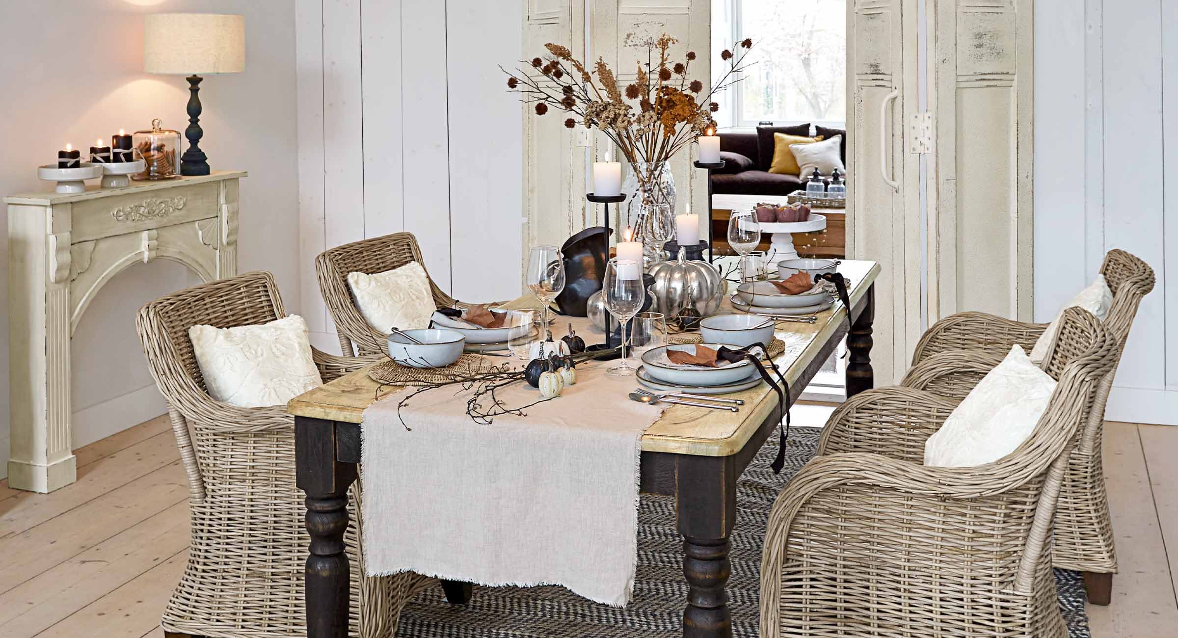 Salle à manger avec chaises en rotin et table en bois décorée de bougies et décorations automnales