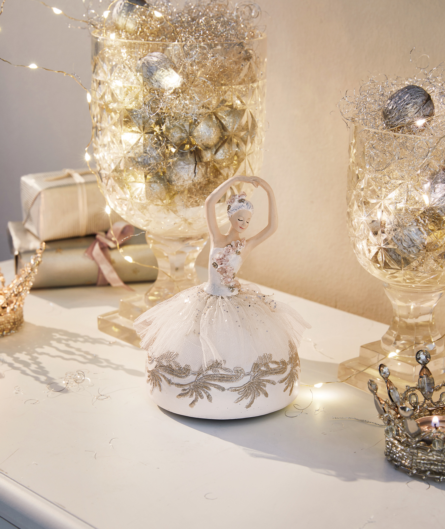 Figurine de ballerine en tissu crème sur une table décorative avec guirlandes lumineuses et cadeaux