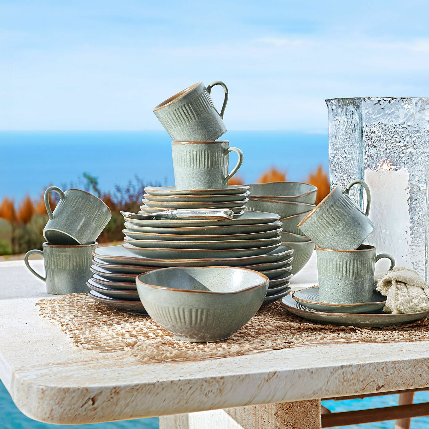 Servies set van 30 Périers Grijs keramisch servies met kopjes en borden op een buitentafel met uitzicht op zee