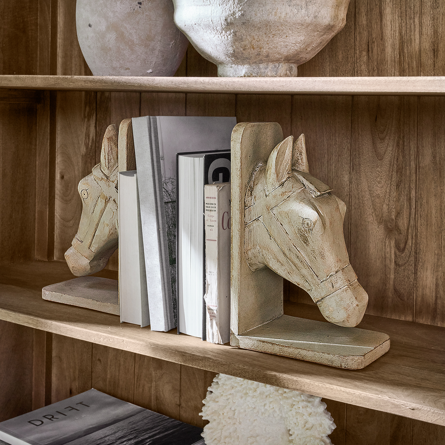 Paire de serre-livres en bois beige sculptés en forme de tête de cheval sur une étagère en bois