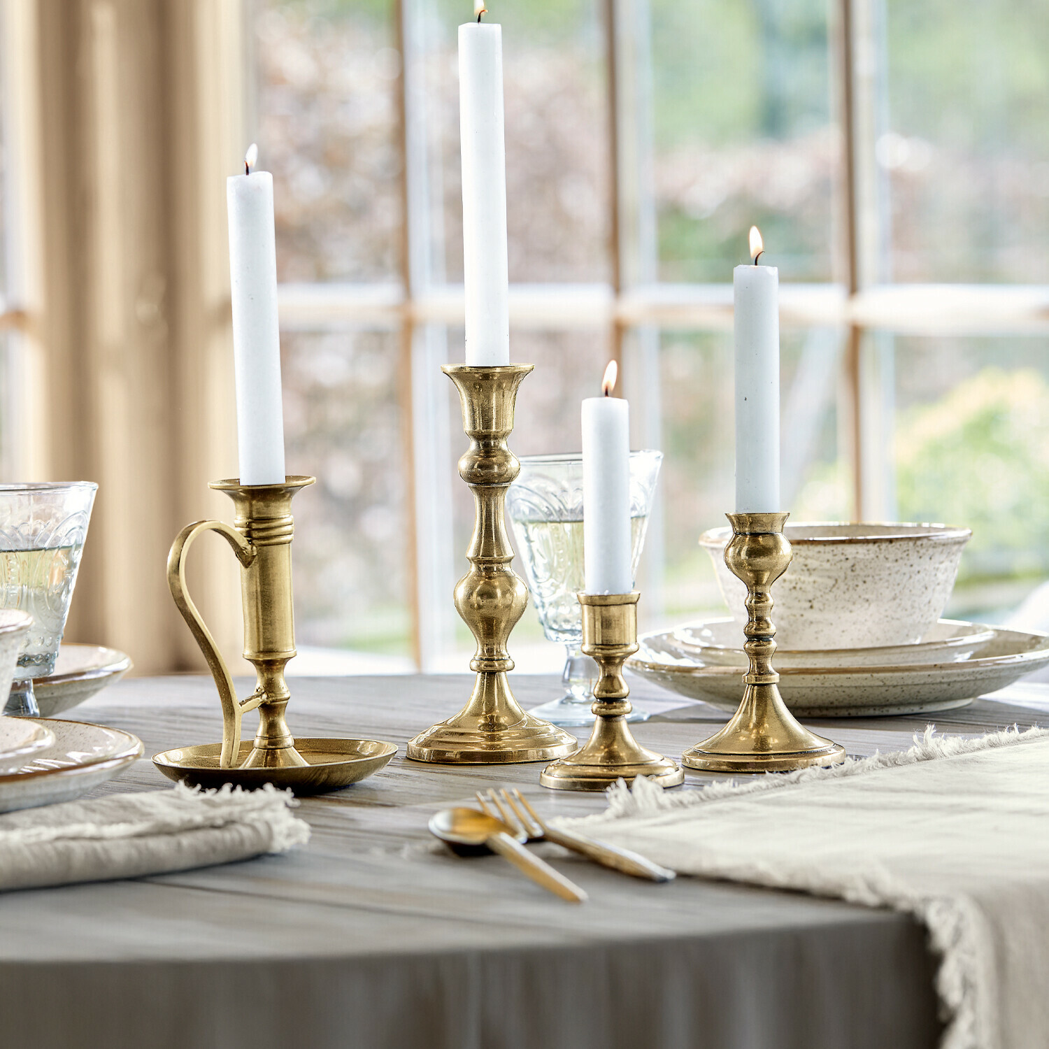 Set van vier messing kandelaars met witte kaarsen op een houten tafel in de eetkamer