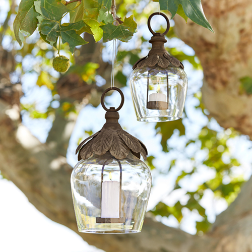 Lanterne en verre suspendue à un arbre avec décorations métalliques et bougies blanches pour jardin