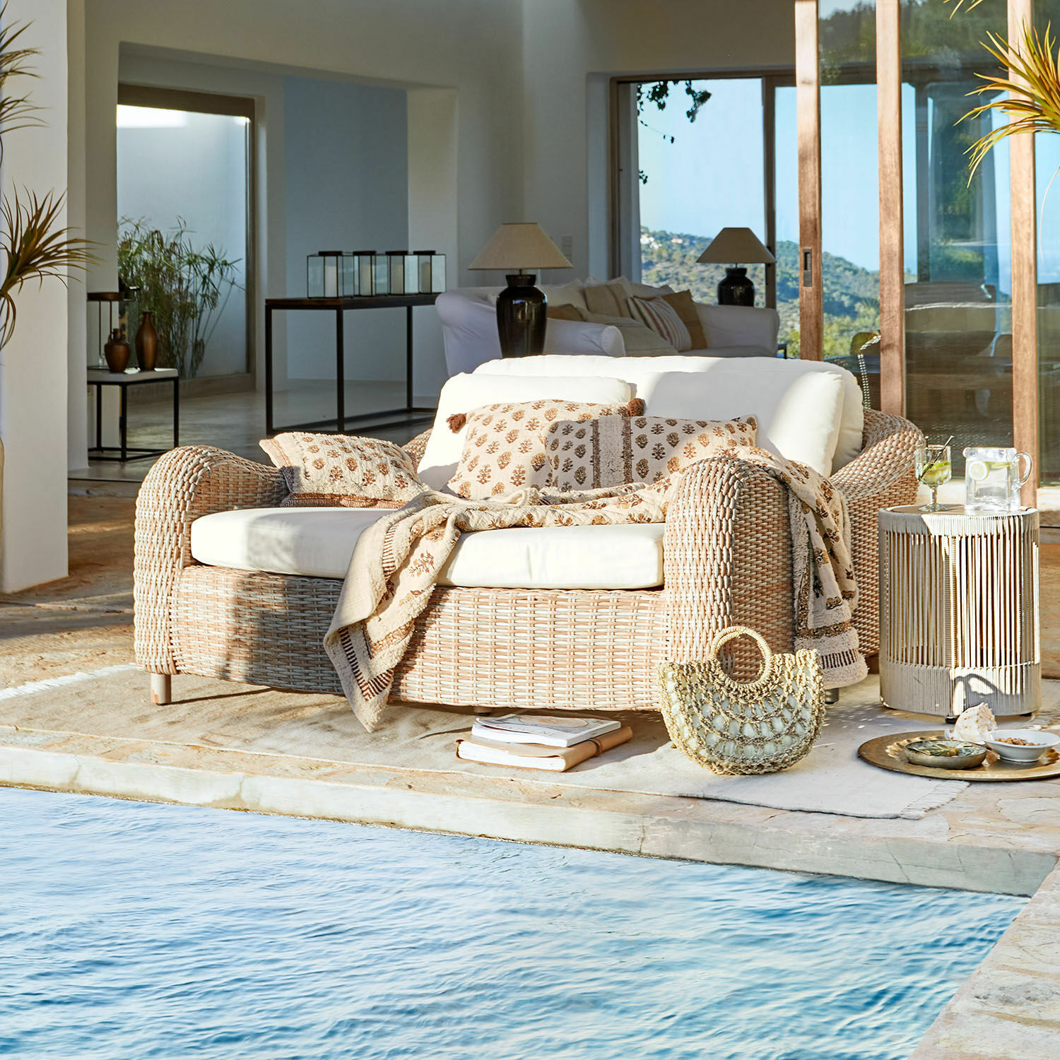 Méridienne Heloite Canapé en rotin naturel avec coussins crème et plaid près de la piscine dans un intérieur moderne