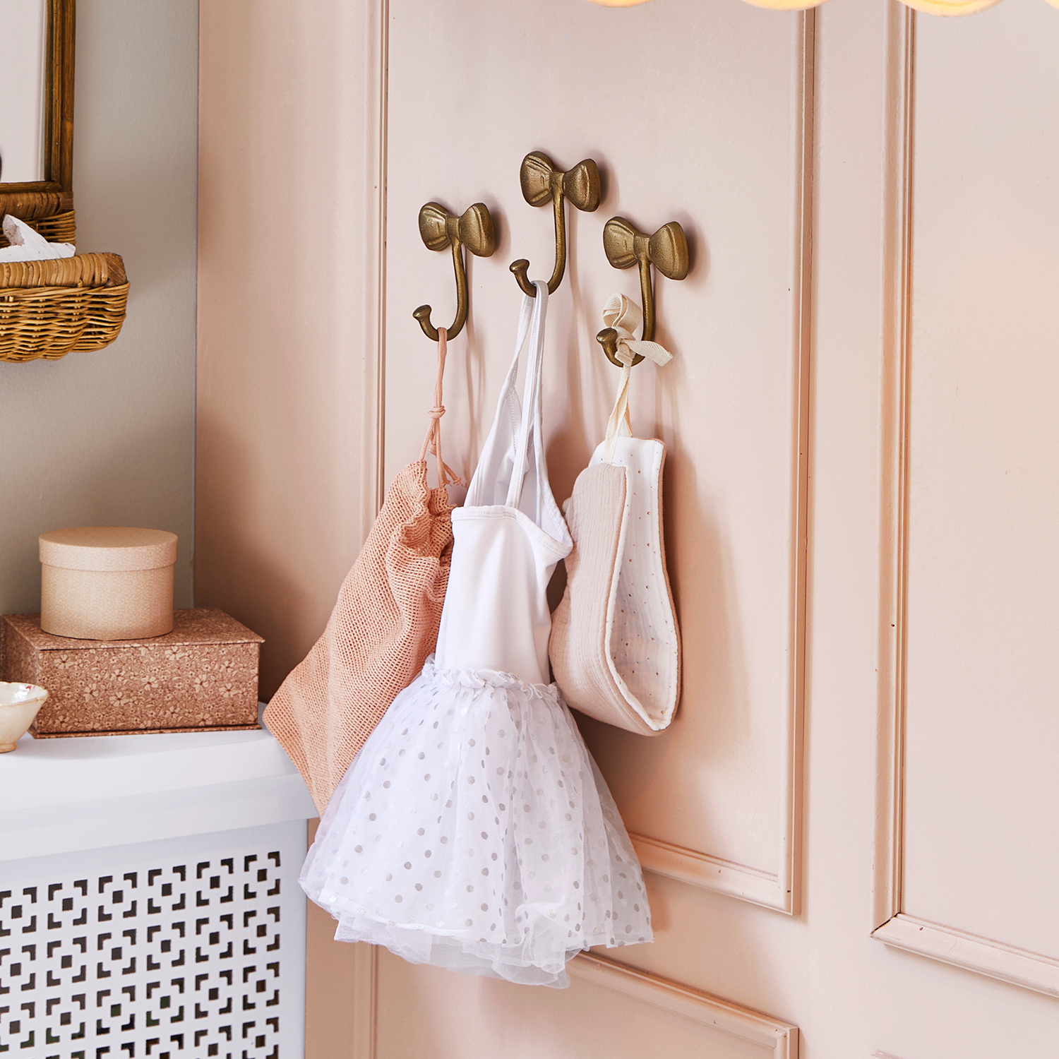 Gouden metalen haakjes in strikvorm aan roze muur met hangende kinderkleding