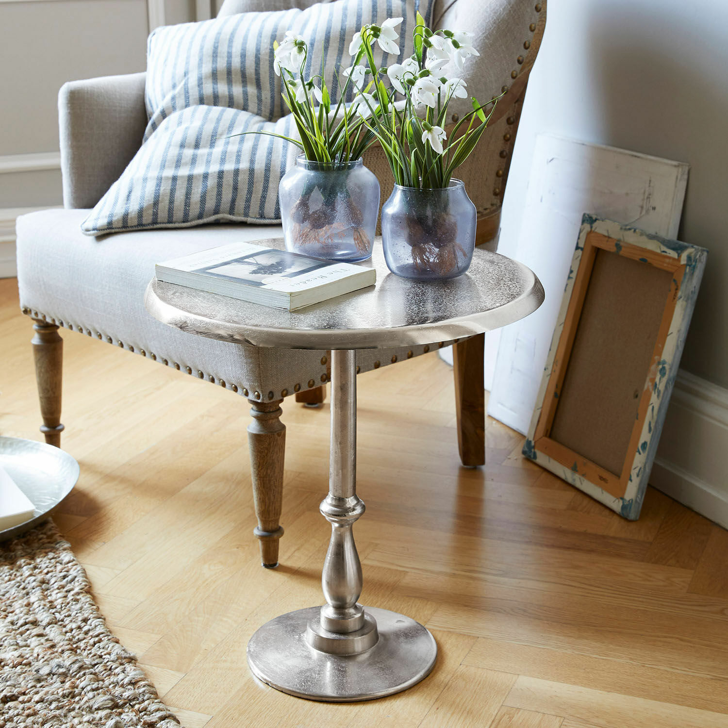 Bijzettafel Eppeville Ronde zilverkleurige metalen bijzettafel met decoratieve vazen en boek in woonkamer