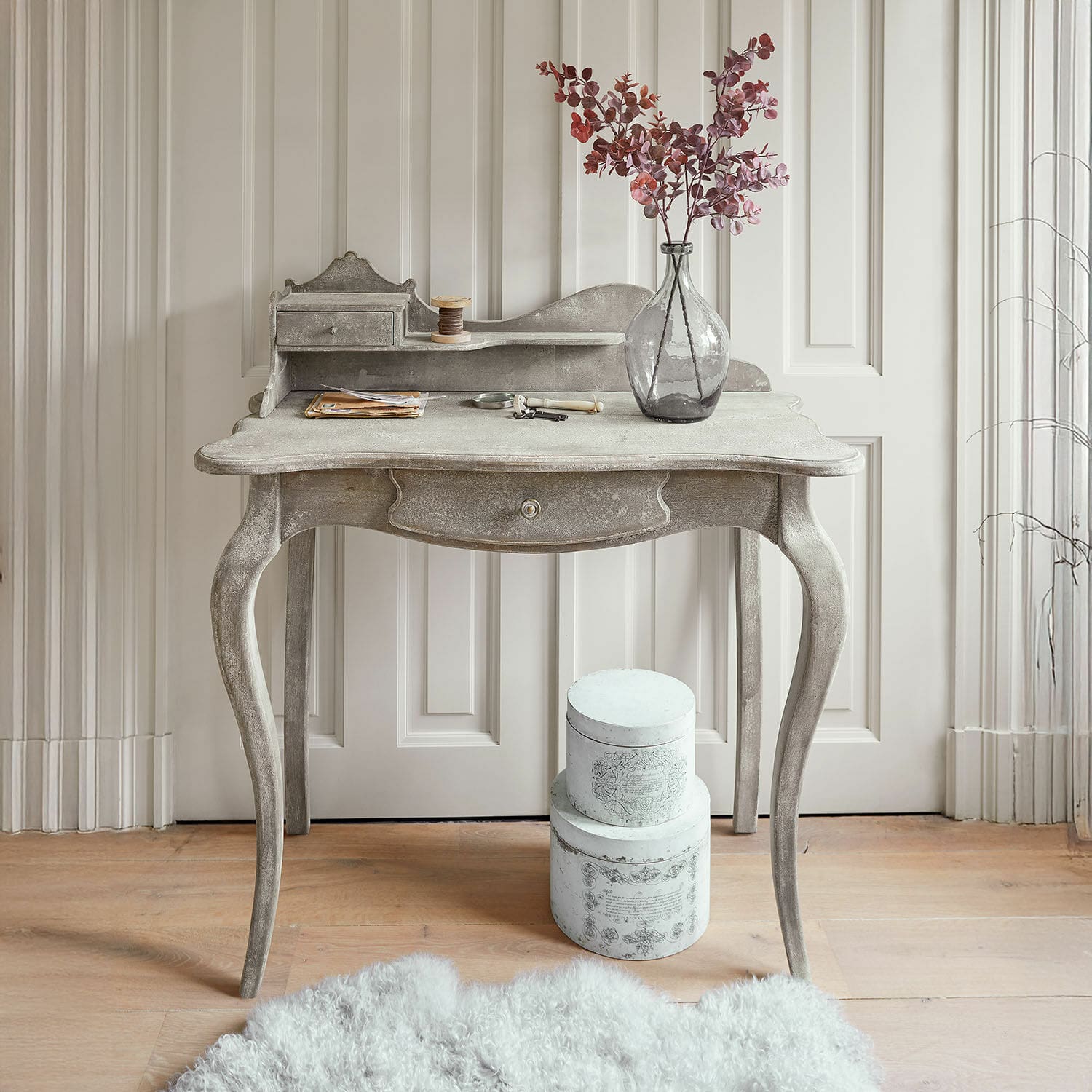 Wandtafel Loustain Stijlvol grijs houten bureau met decoratieve vaas en dozen op de vloer, vintage meubelstuk