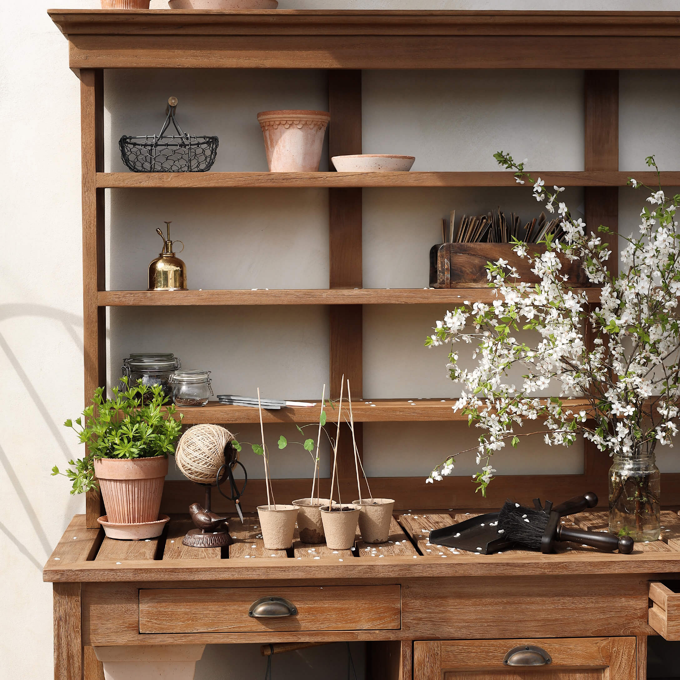 Table de jardin en bois avec pots, outils de jardinage et branches fleuries dans un bocal en verre