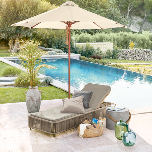 Chaise longue de jardin beige avec coussins et parasol près de la piscine, décorations en rotin et verre