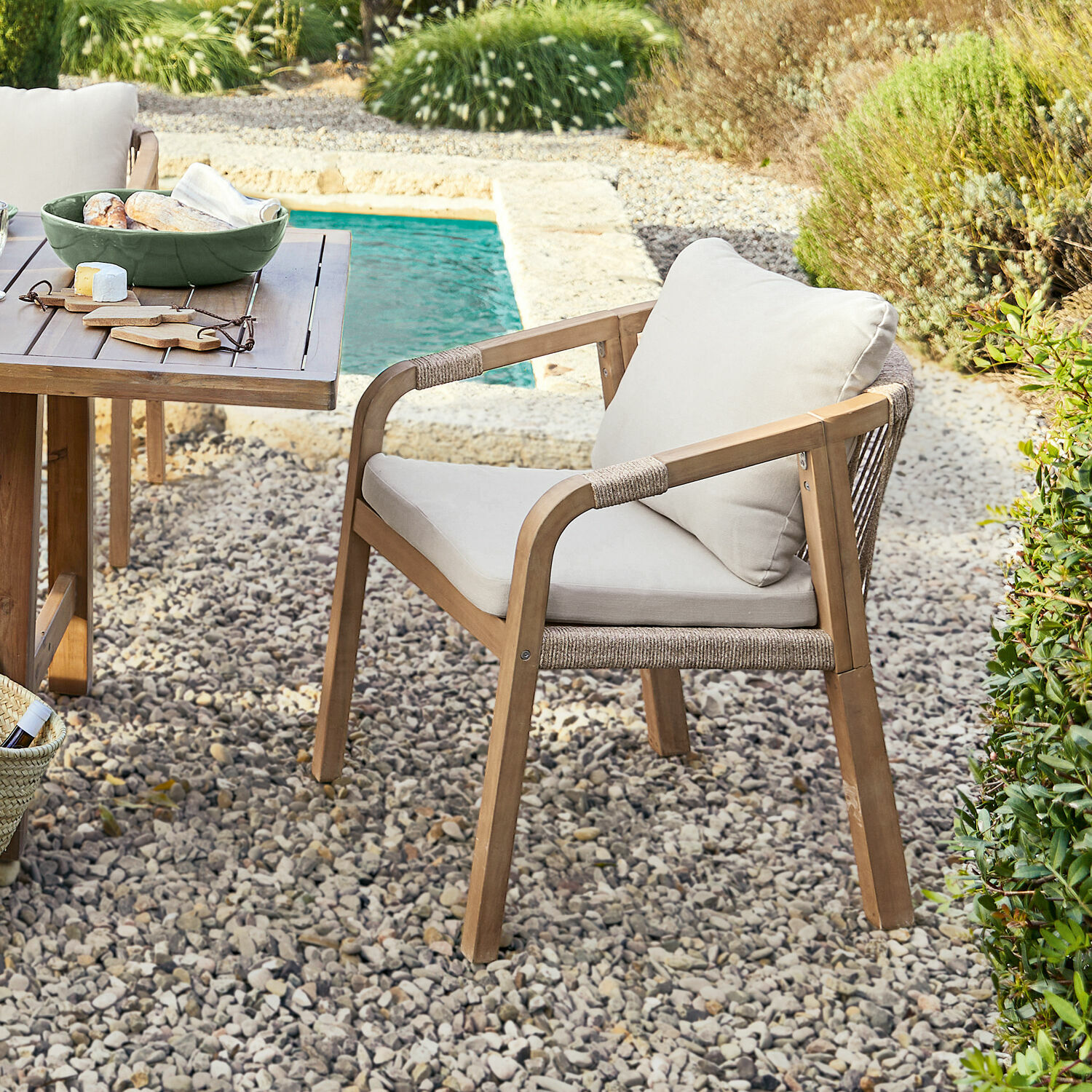 Chaise de jardin en bois avec coussins clairs sur patio en gravier près de la piscine