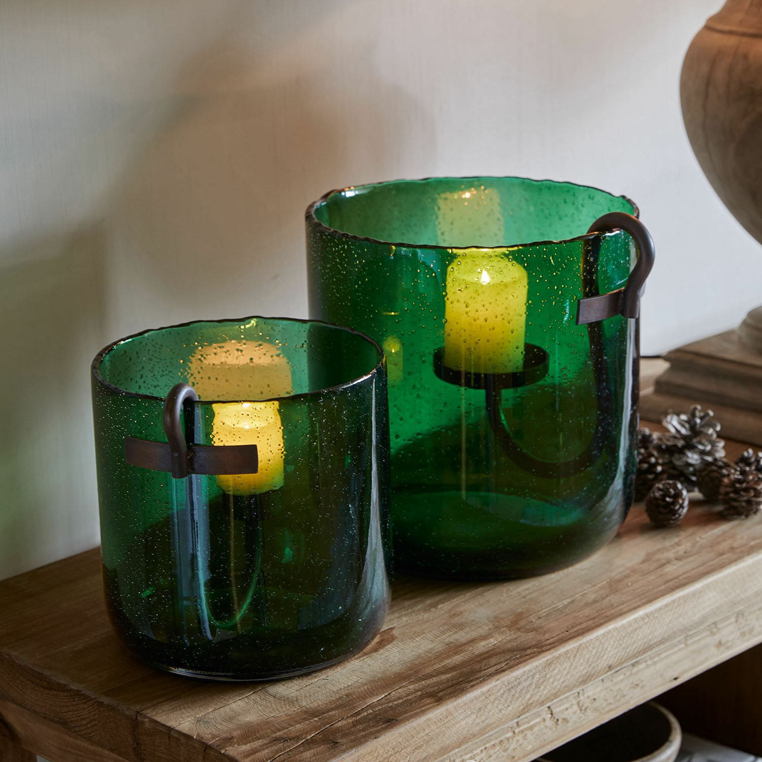 Windlicht set van 2 Ylva Set van twee groene glazen windlichten met metalen handvatten op een houten tafel