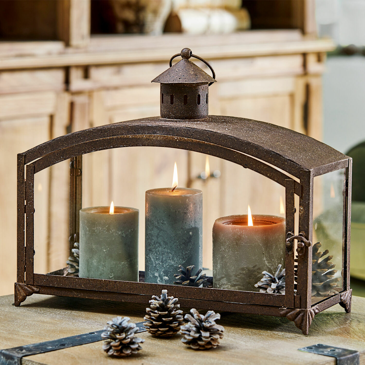 Lanterne Miora Lanterne en métal avec trois bougies vertes et pommes de pin sur une table en bois, décoration intérieure