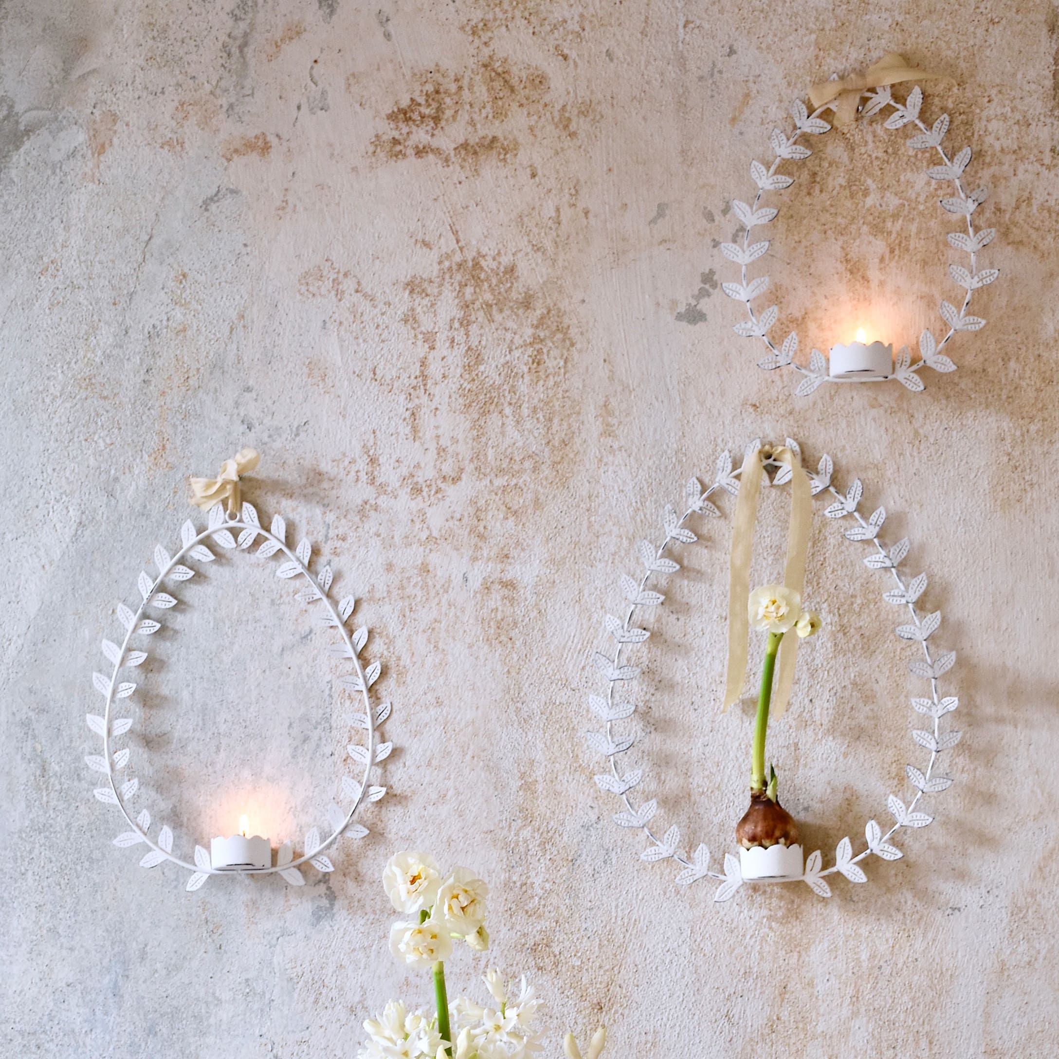 Décorations murales blanches en métal en forme d'œufs avec feuilles, bougies et fleurs sur mur pastel