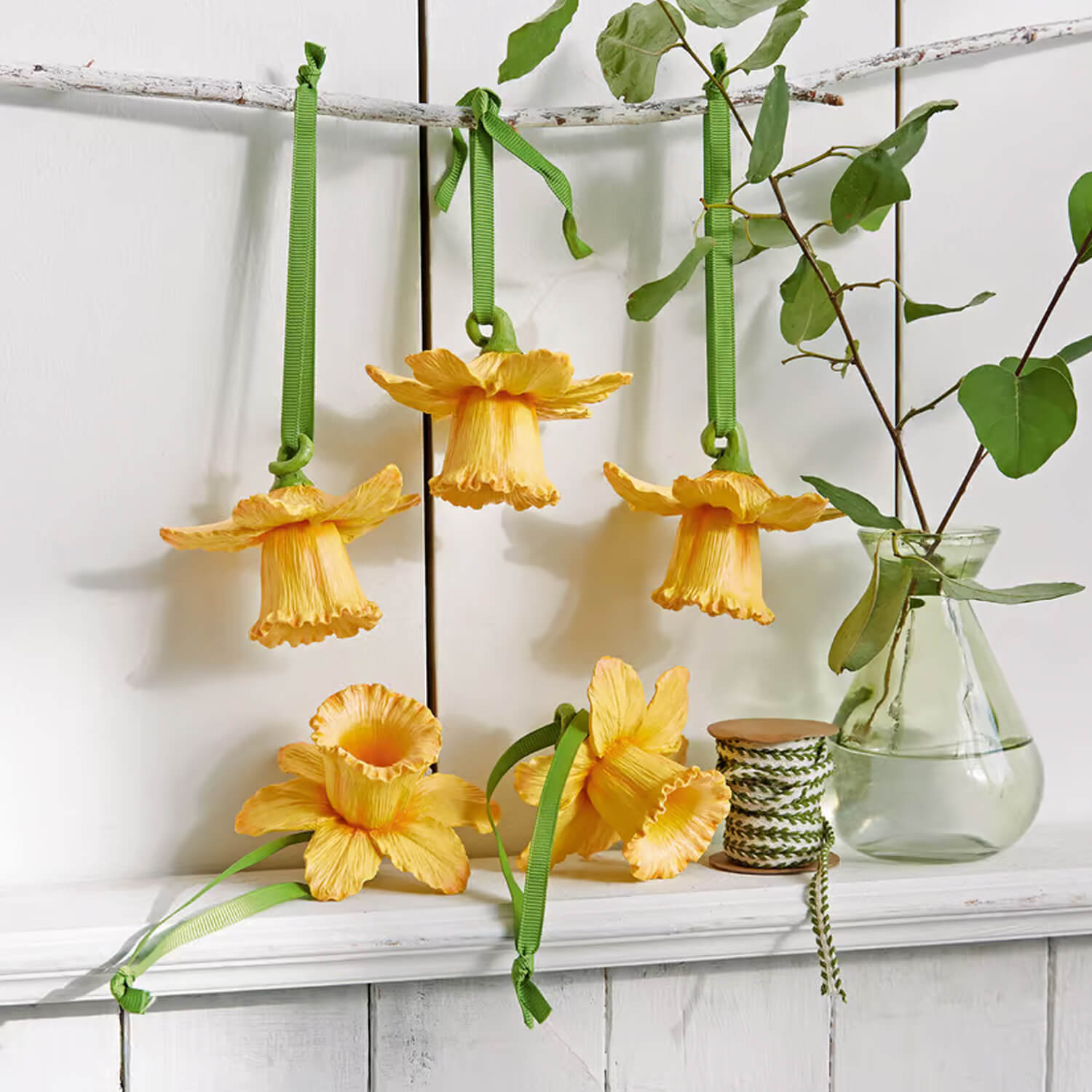 Gele bloemdecoraties met groene linten aan witte plank, lenteversiering voor interieur