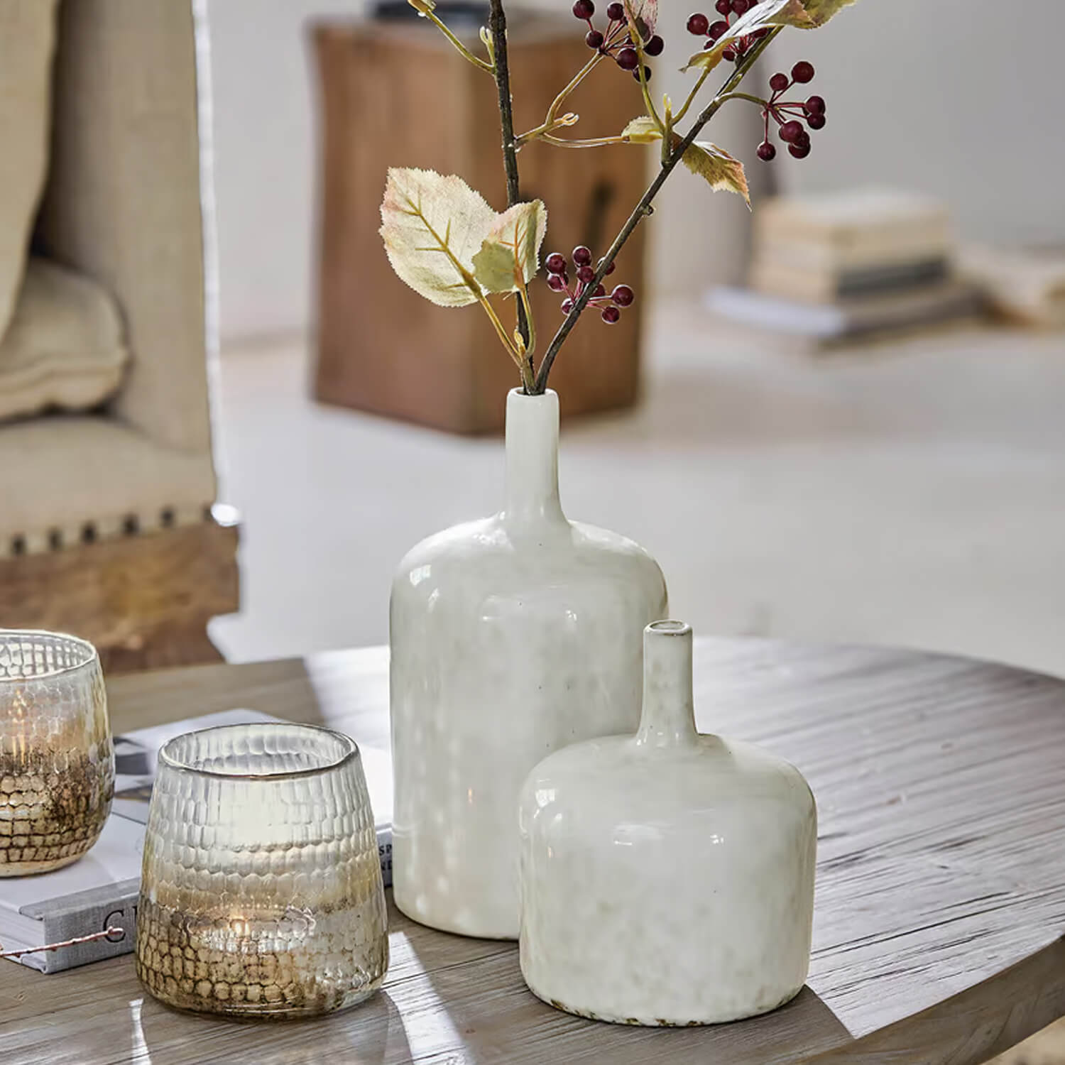 Deux vases en céramique blanche sur une table en bois avec branches décoratives et bougies