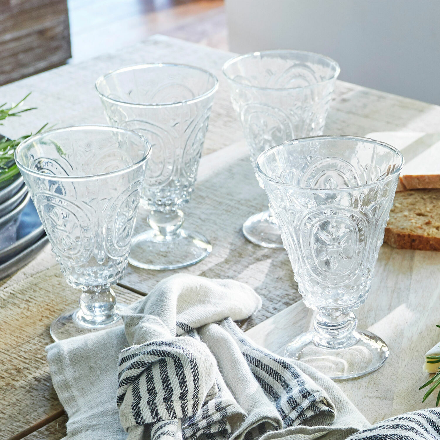 Set van vier doorzichtige glazen met decoratief patroon op houten tafel met stof en brood