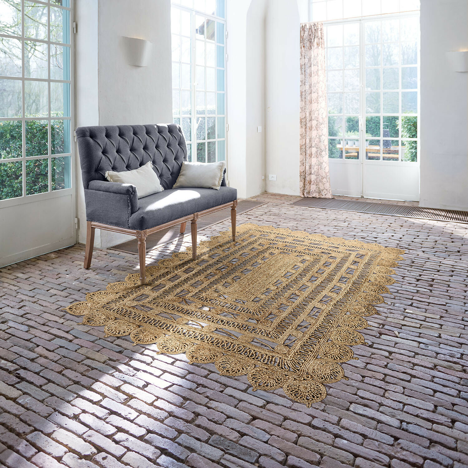 Vloerkleed Livadia Grijze gestoffeerde bank met houten poten in lichte kamer met jute vloerkleed op bakstenen vloer