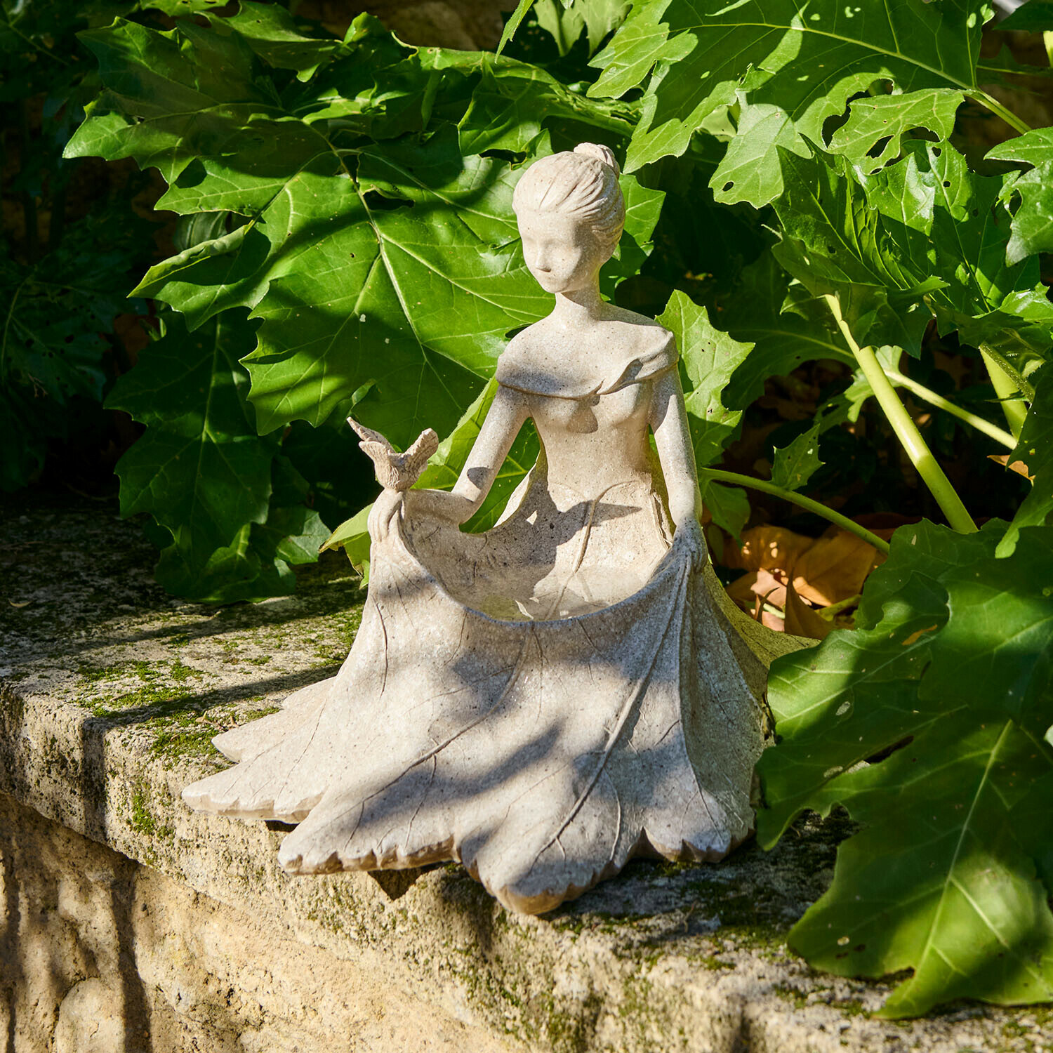 Statue en pierre d'une femme tenant un oiseau, décoration de jardin posée sur un muret en pierre