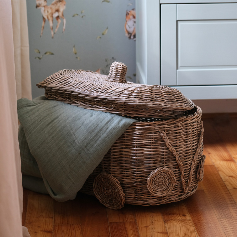 Panier en osier en forme de voiture avec une couverture verte sur un sol en bois dans une chambre d'enfant