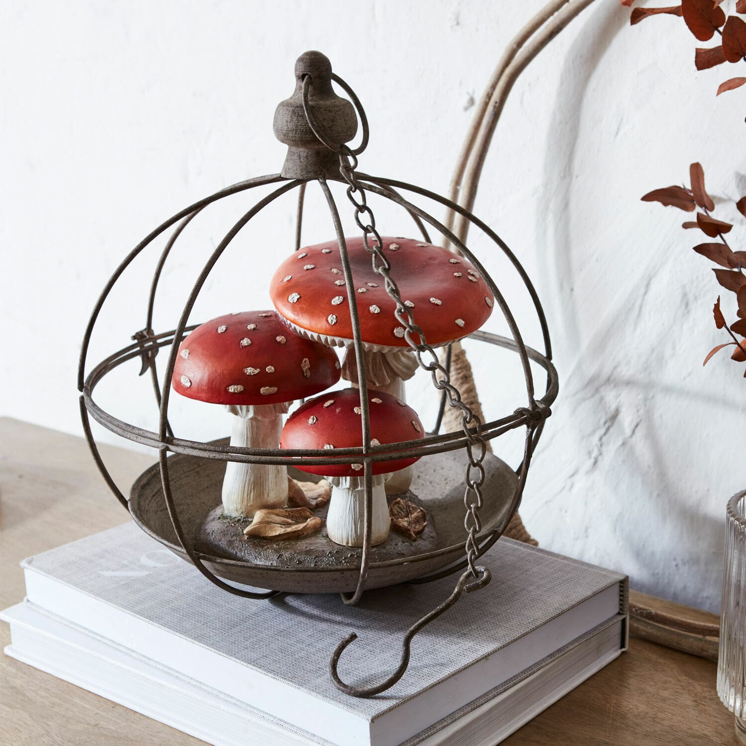 Volière Valère Decoratie met rode vliegenzwammen in metalen kooi op boeken op houten tafel