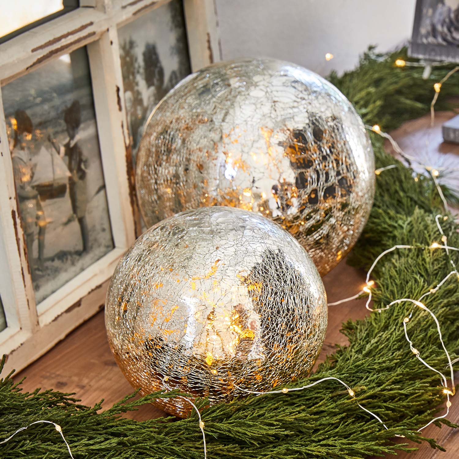 Twee decoratieve glazen bollen met gebarsten oppervlak en warm licht tussen groene takken